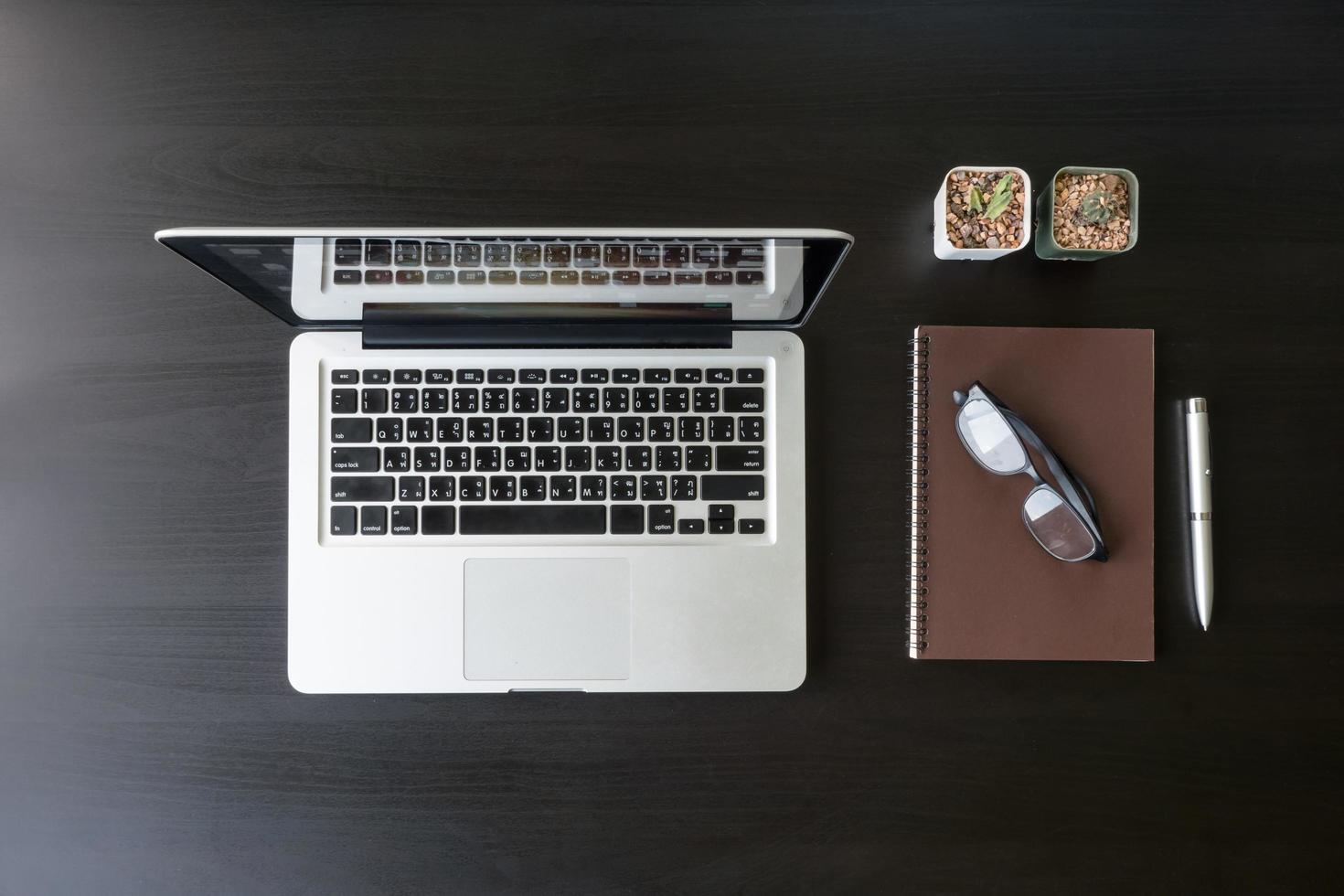 Top view of Laptop with notebook, glasses, pen and cactus on black desk. photo