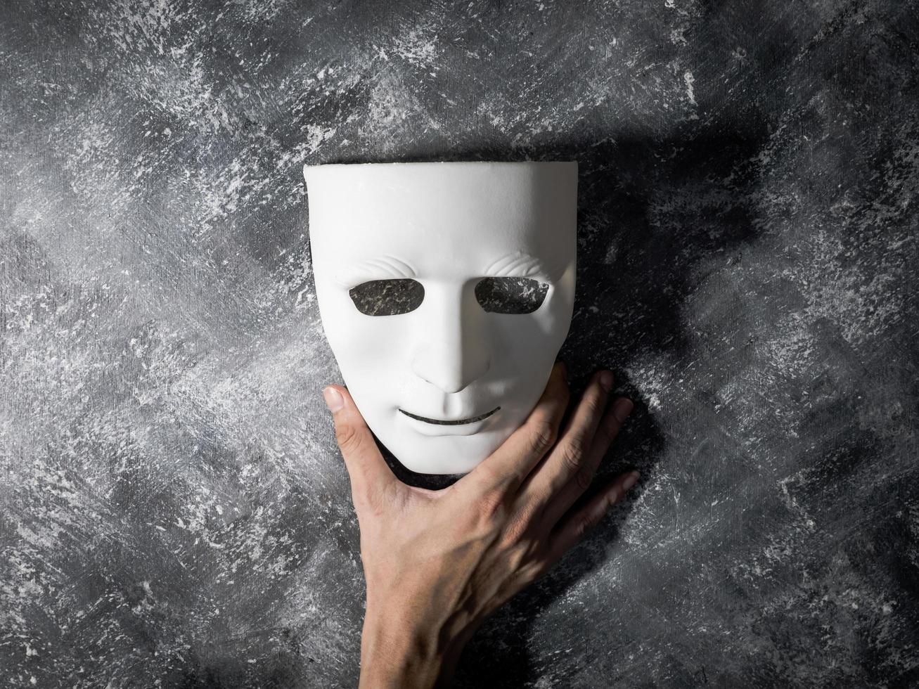 Hand holding white mask on gray grunge background. photo