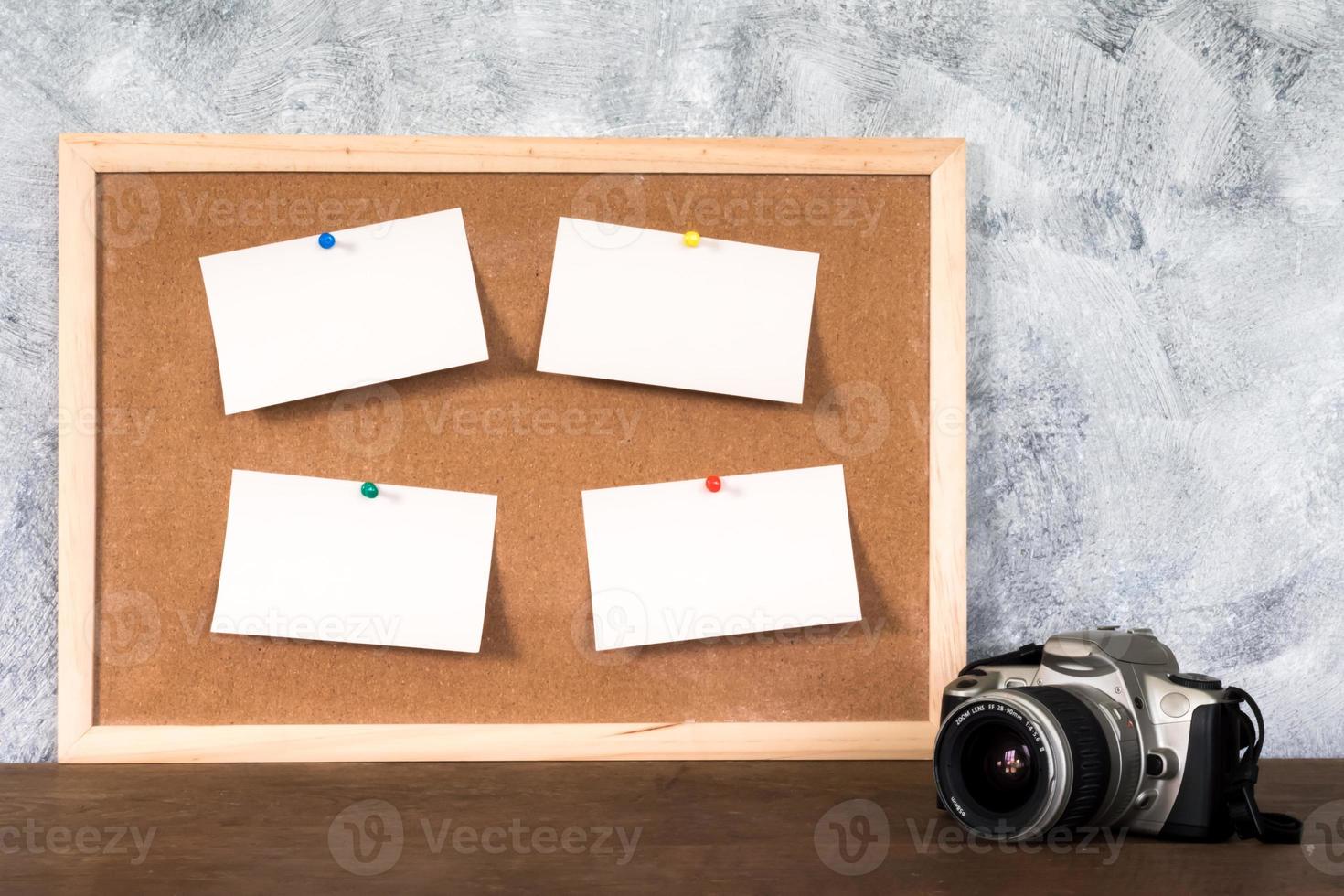 Blank papers pin up on cork board and camera over wooden table with textured background. photo