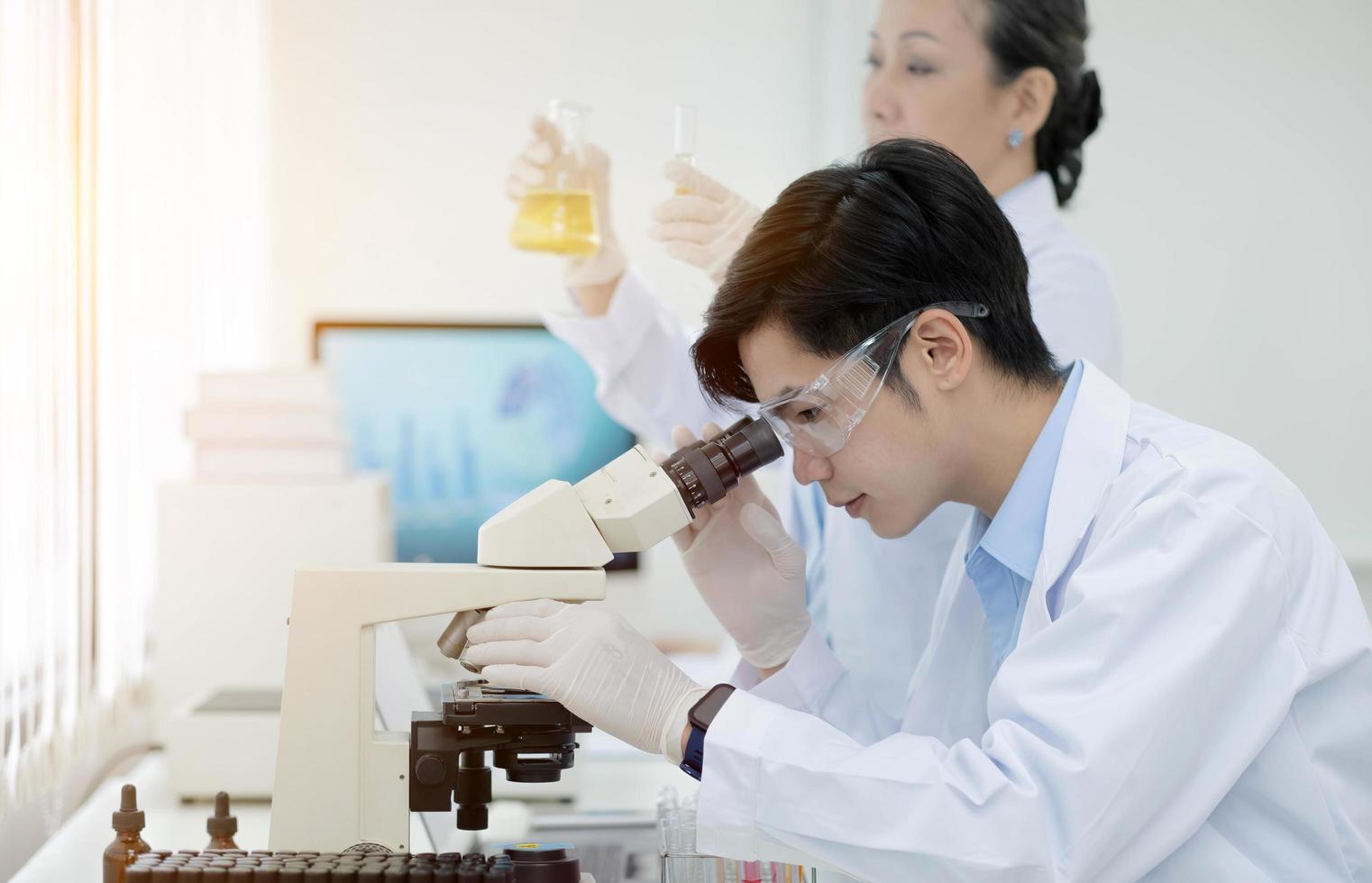 biochemical research scientist team working with microscope for coronavirus vaccine development in pharmaceutical research labolatory, selective focus photo