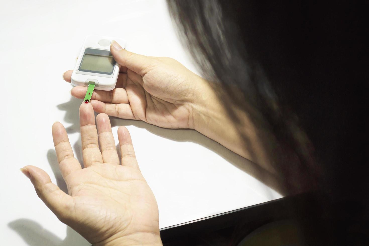 la mujer está controlando la diabetes usando un kit de control de sangre aislado sobre blanco foto