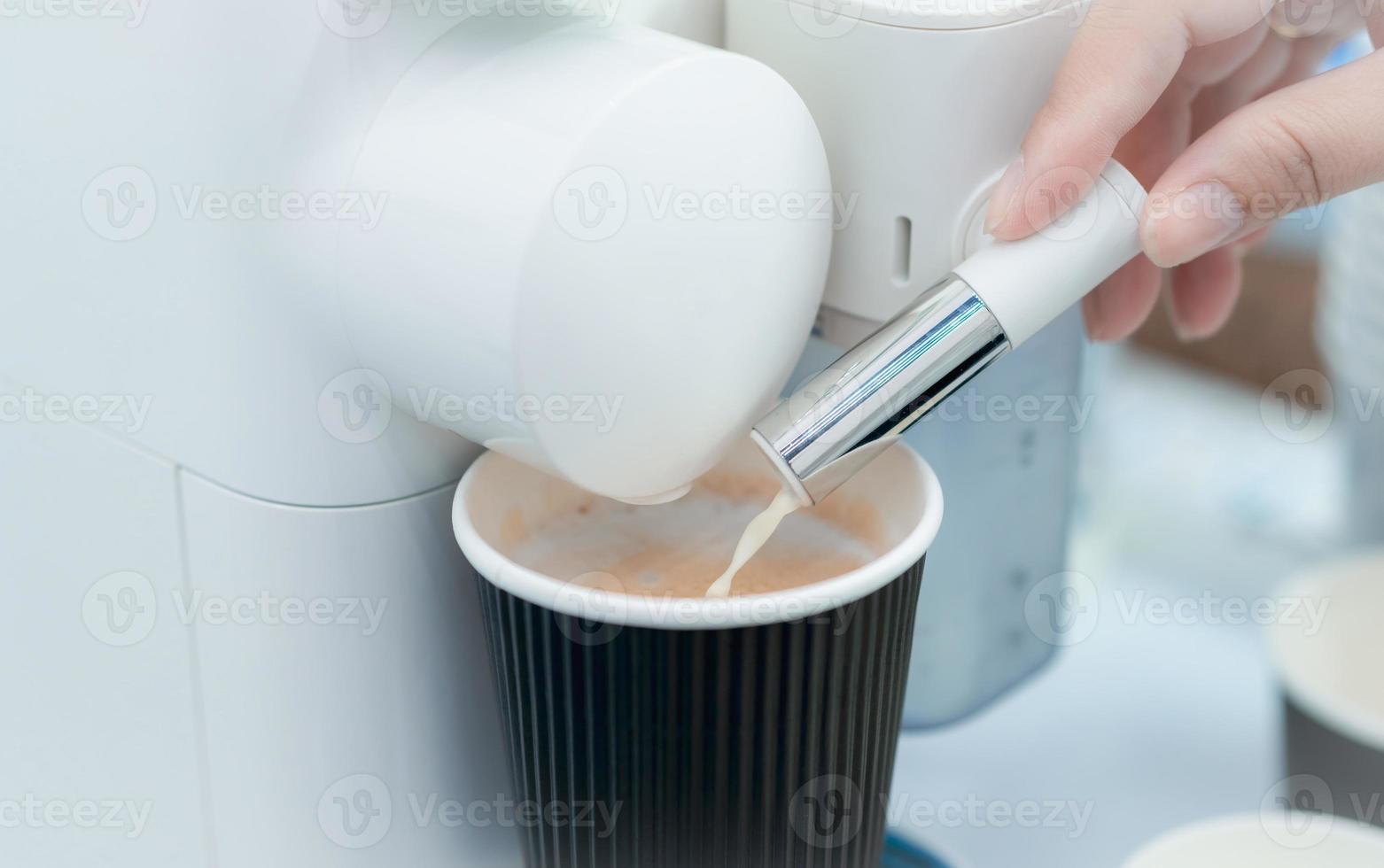 Woman making a cup of hot coffee with capsule coffee machine. Woman hand holding frothed milk dispenser of capsule coffee machine on table. Latte coffee maker. Morning drink. Modern home equipment. photo