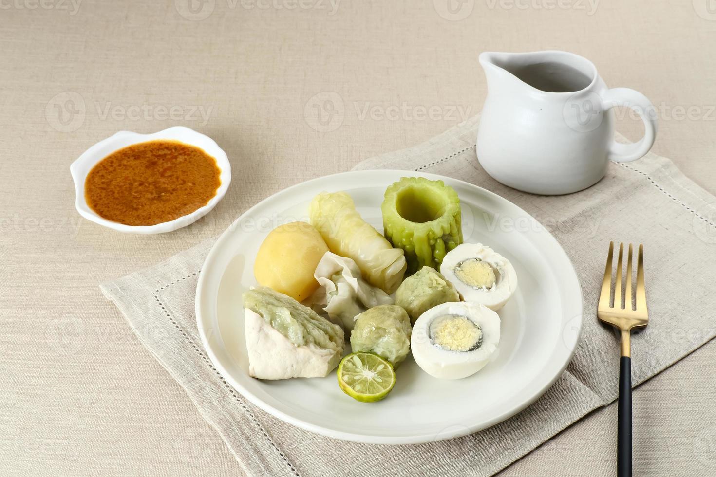 siomay bandung, albóndigas al vapor con huevo cocido, tofu, patatas y rollo de col. Comida callejera tradicional indonesia con salsa de cacahuete y salsa de soja, servida con lima verde. foto