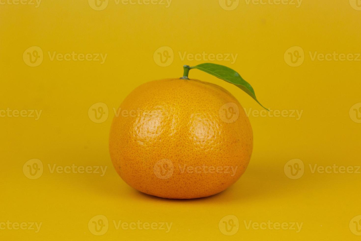 An Orange fruit with green leaf isolated on yellow background. One orange fruit with leaf stand on isolating concept for ads design photo