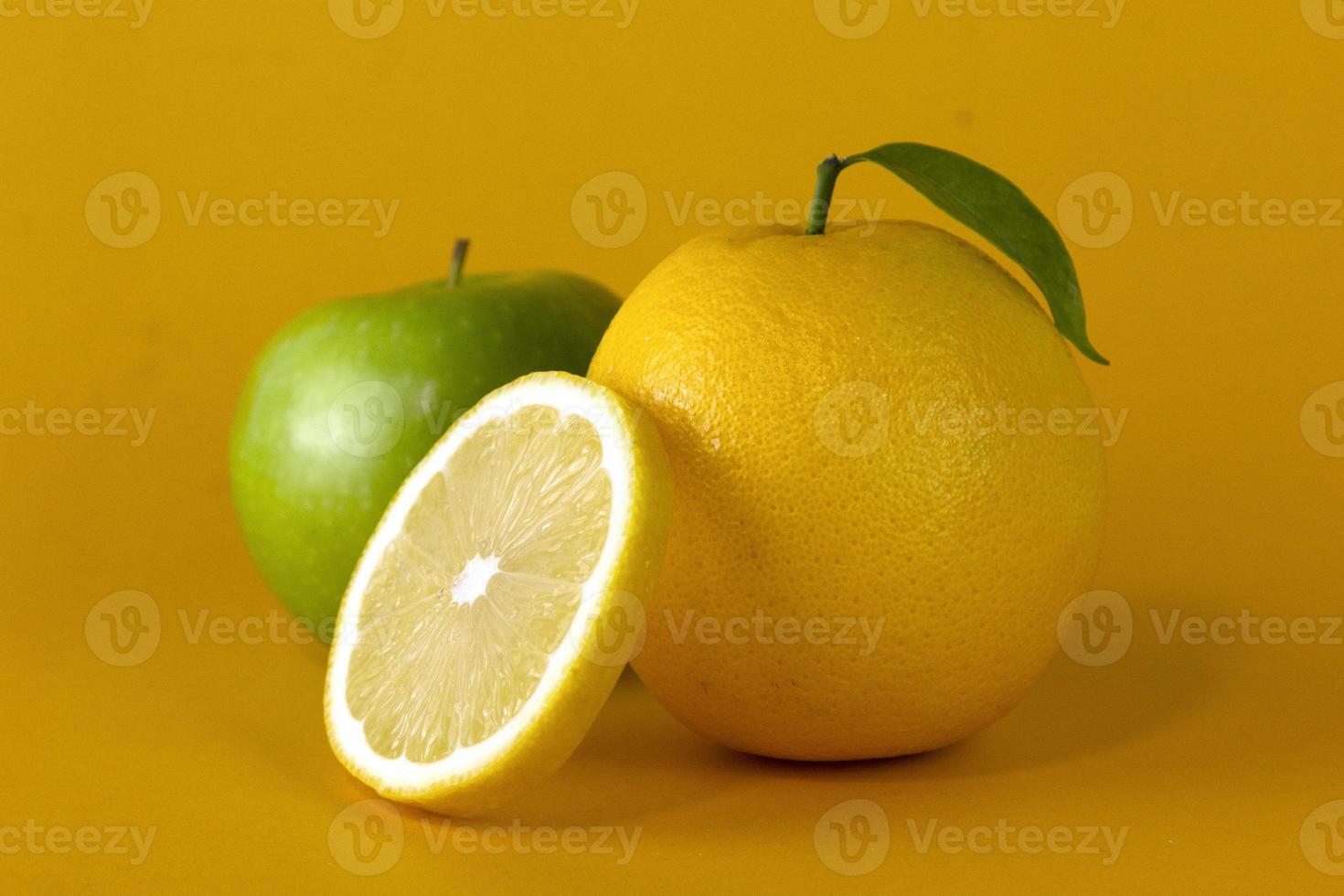 A green apple with lemon fruits and a Lemon slice with leaf isolated on yellow background, for concept of healthy fruit design photo