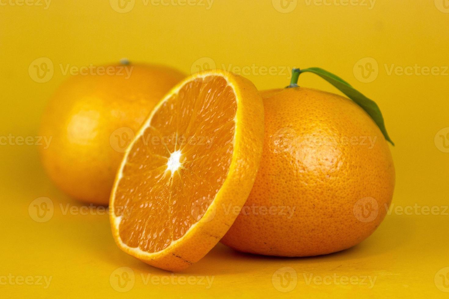 jugosa fruta naranja con hoja aislada. y naranja entera, rebanada, hojas en blanco. rodaja de naranja con diseño aislado sobre fondo amarillo foto