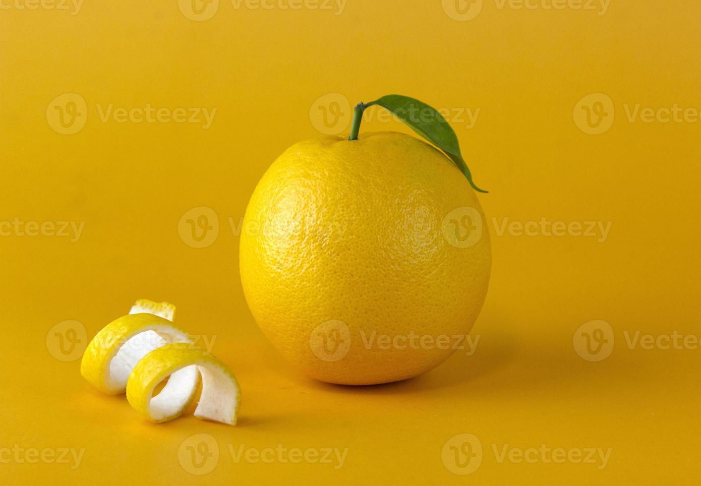 A yellow lemon fruit with leaf and peel slice isolated on yellow background photo