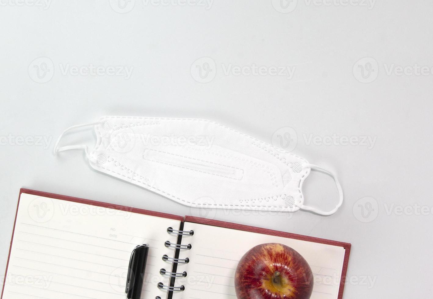 concepto de regreso a la escuela con materiales educativos, mascarilla, cuaderno, manzana, bolígrafo aislado en fondo blanco. plantilla de conceptos de vista superior foto