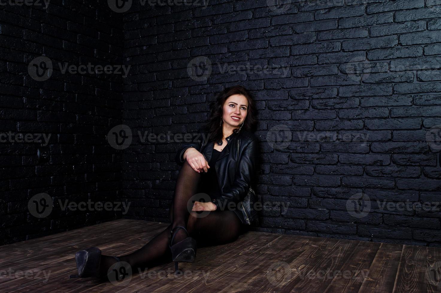 Studio portrait of sexy brunette girl in black leather jacket against brick wall. photo