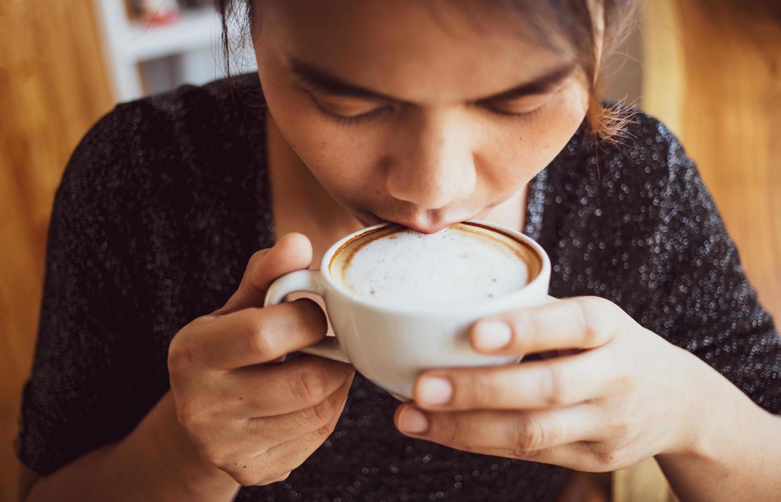 el primer plano de una hermosa chica que huele y bebe café caliente sintiéndose bien en el café disfruta de su capuchino matutino con café con espuma de leche foto