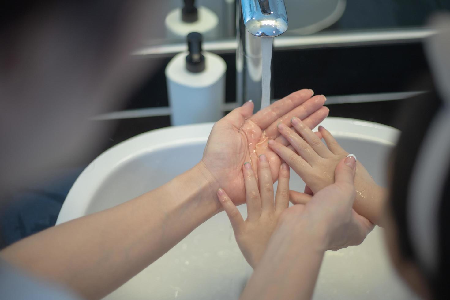 Mother teaching her daughter to wash her hands with soap photo