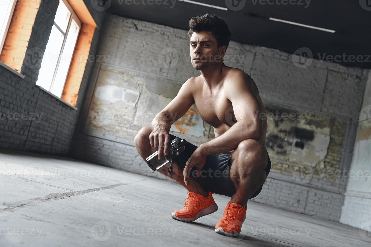 Confident muscular man holding bottle with water while relaxing after training in gym photo