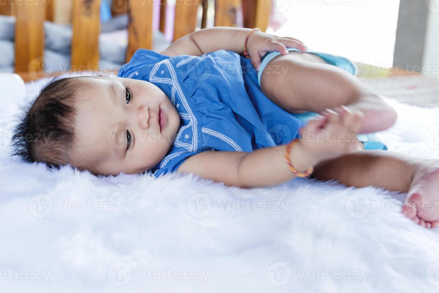 A beautiful 6 month old baby with big eyes lies on the bed. photo