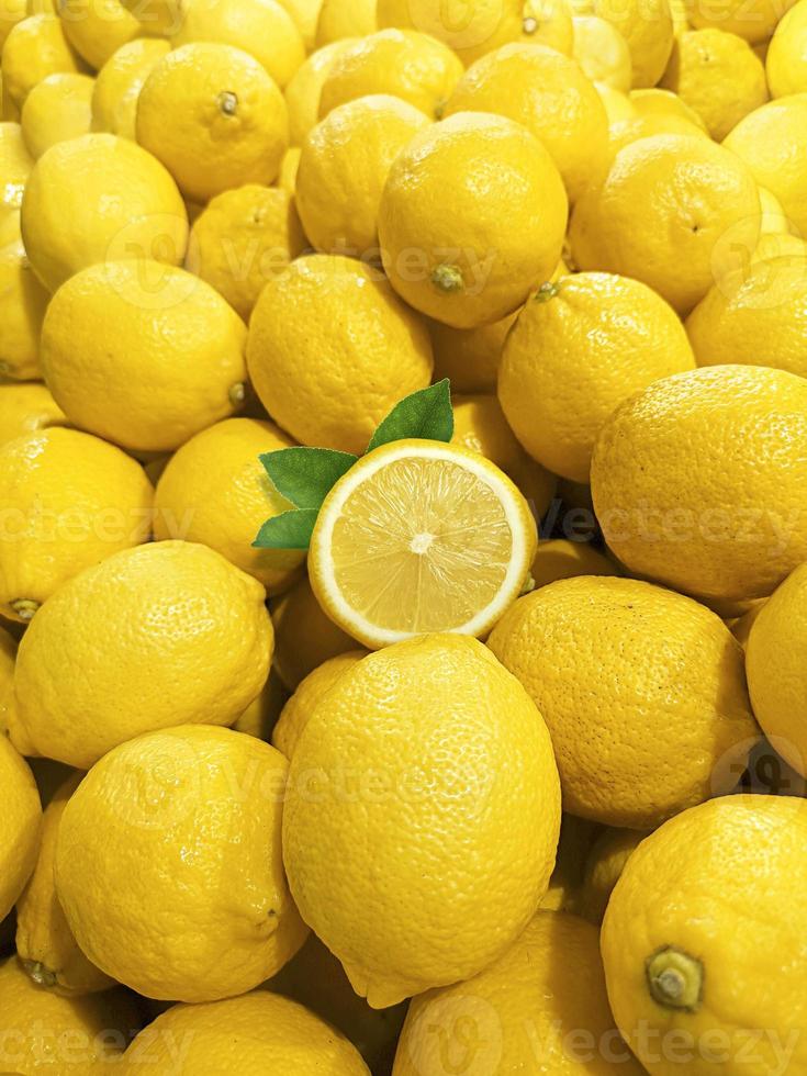 rebanada madura de cítricos de limón amarillo con hojas sobre fondo de limones amarillos maduros foto