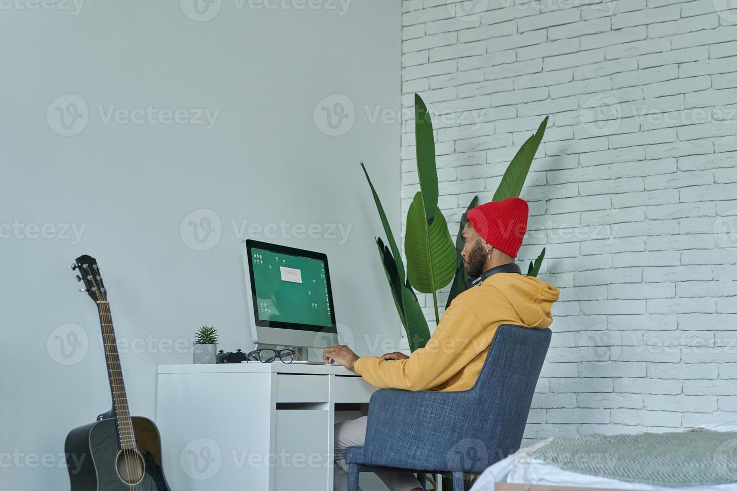 Young African man using computer while sitting at his working place at home photo