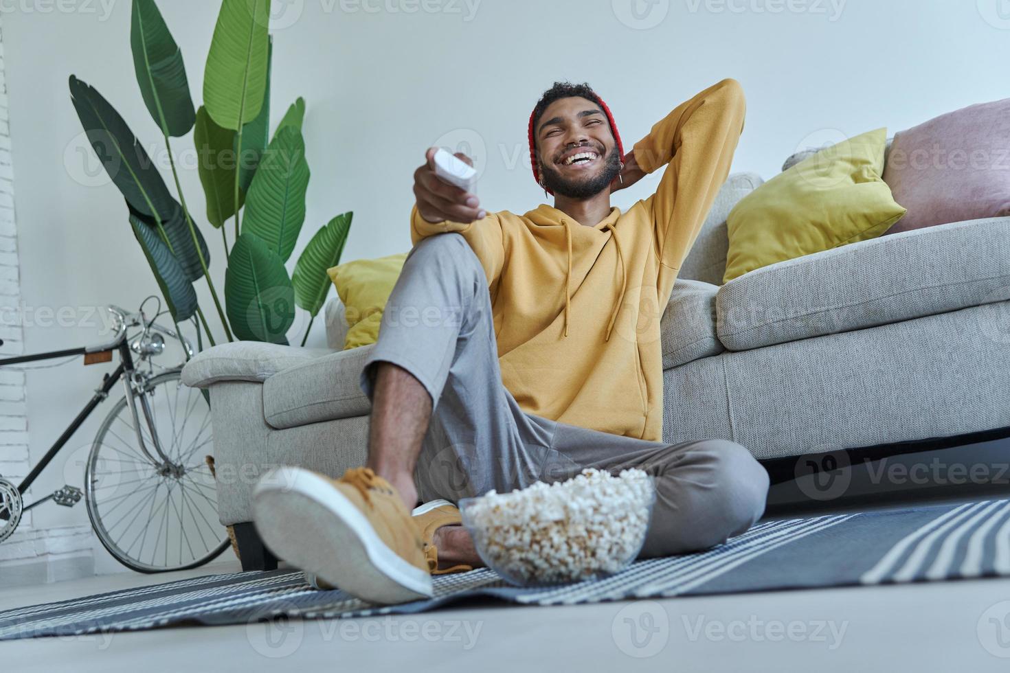 Relaxed young African man watching TV while sitting on the floor at home photo