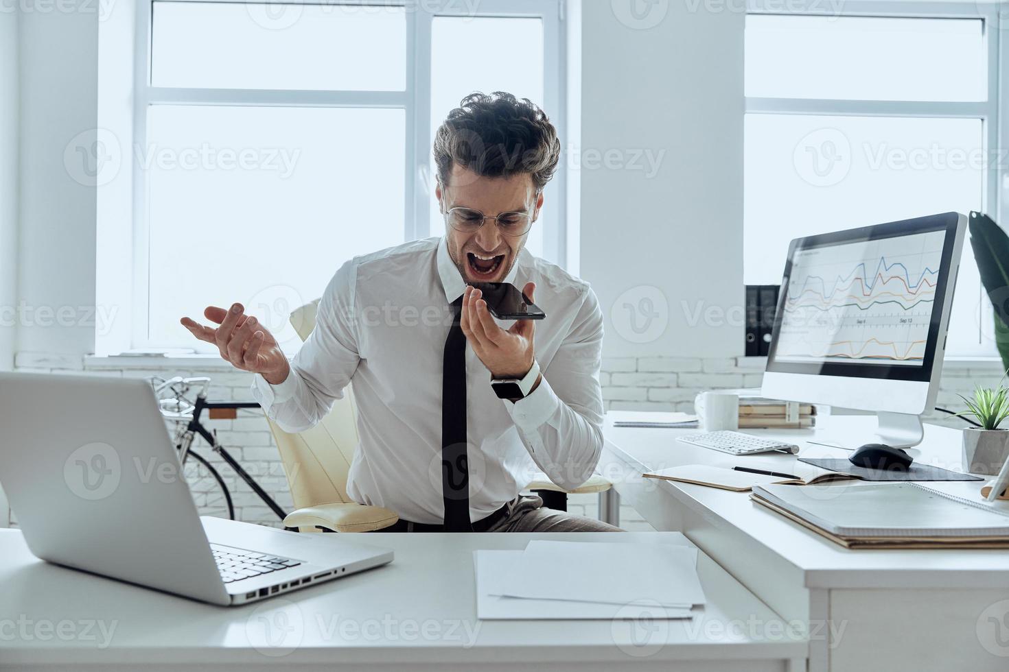 un joven furioso que usa un altavoz mientras grita al teléfono móvil en la oficina foto