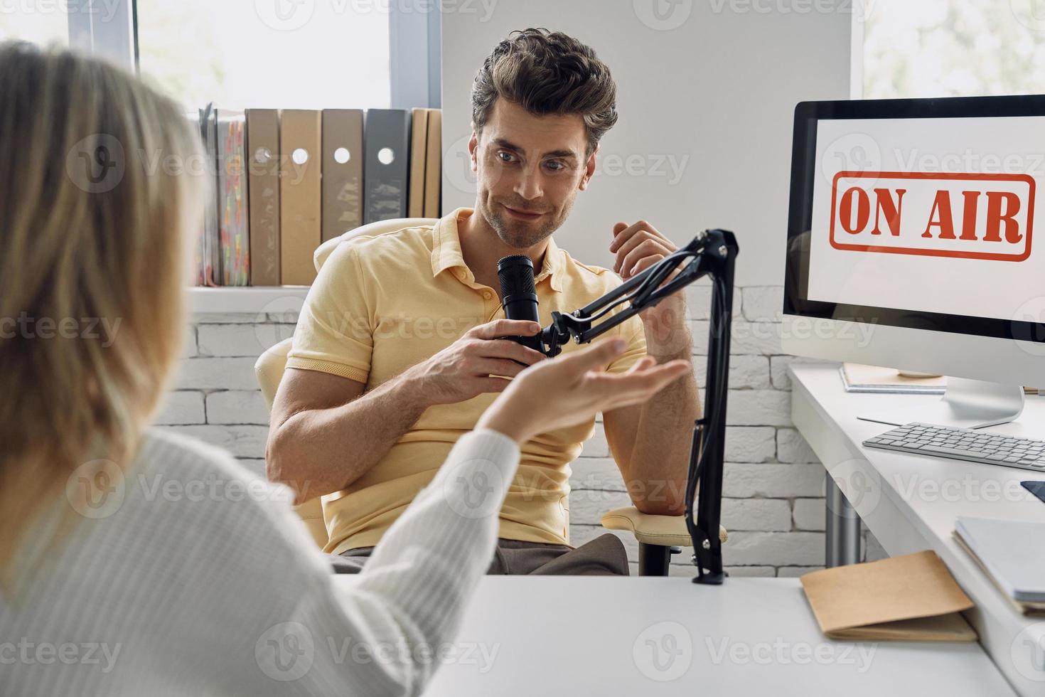 Handsome young man recording podcast interview with guest in studio photo