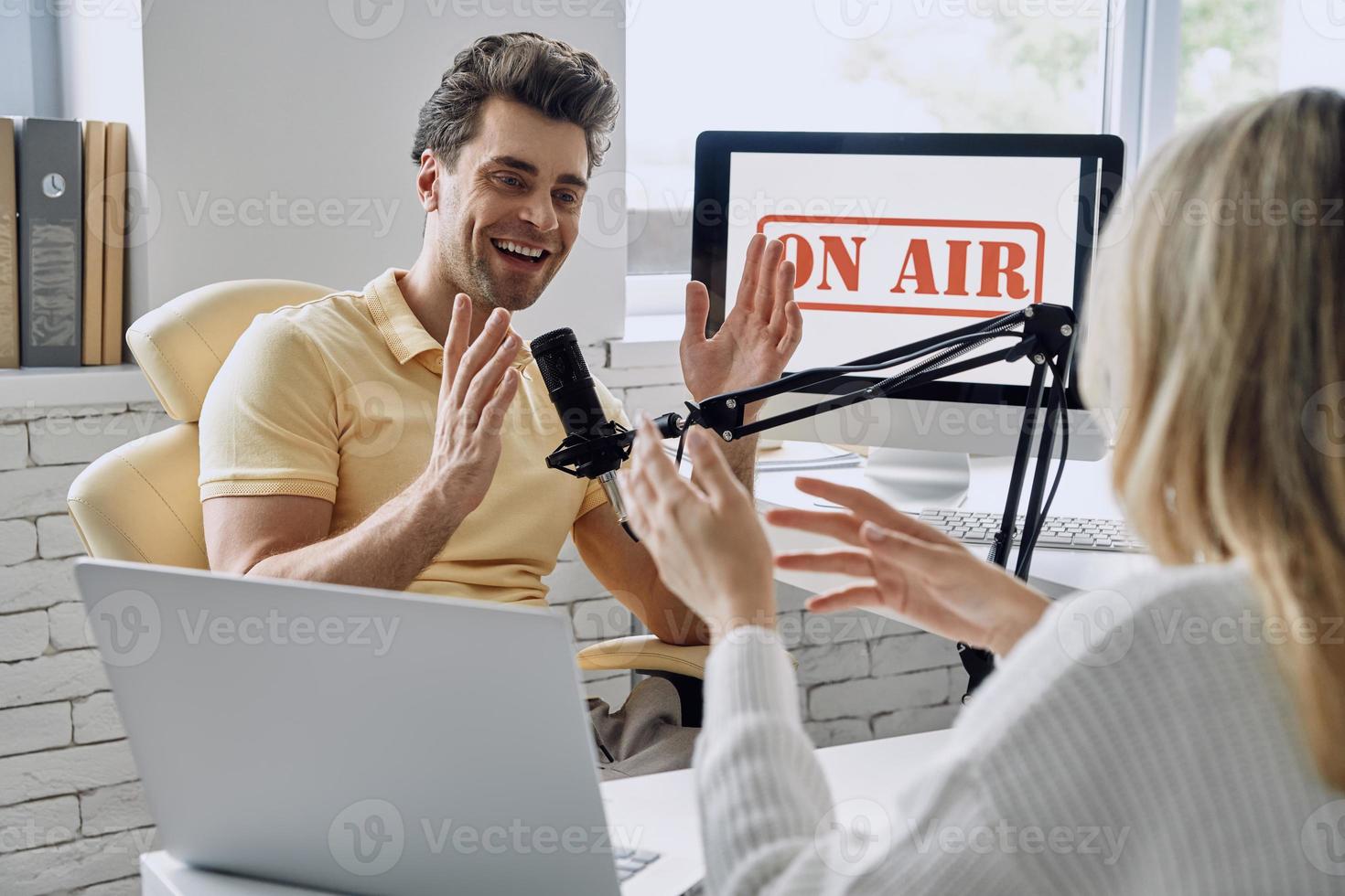 Happy young man gesturing while recording podcast interview with guest in studio photo