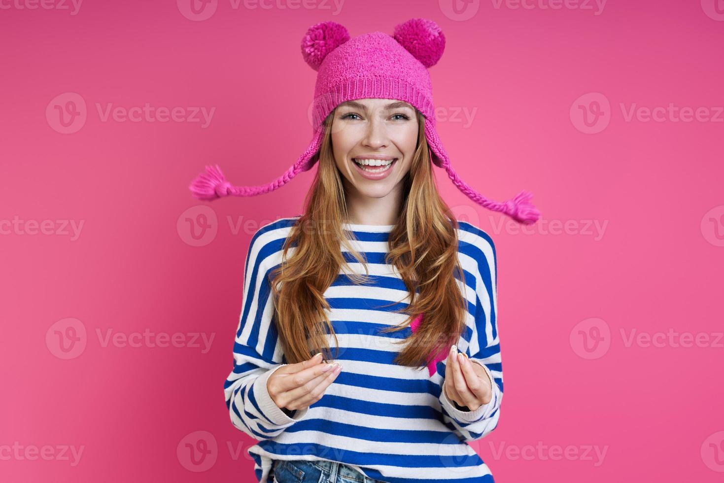 Playful young woman in pink hat smiling while standing against colored background photo