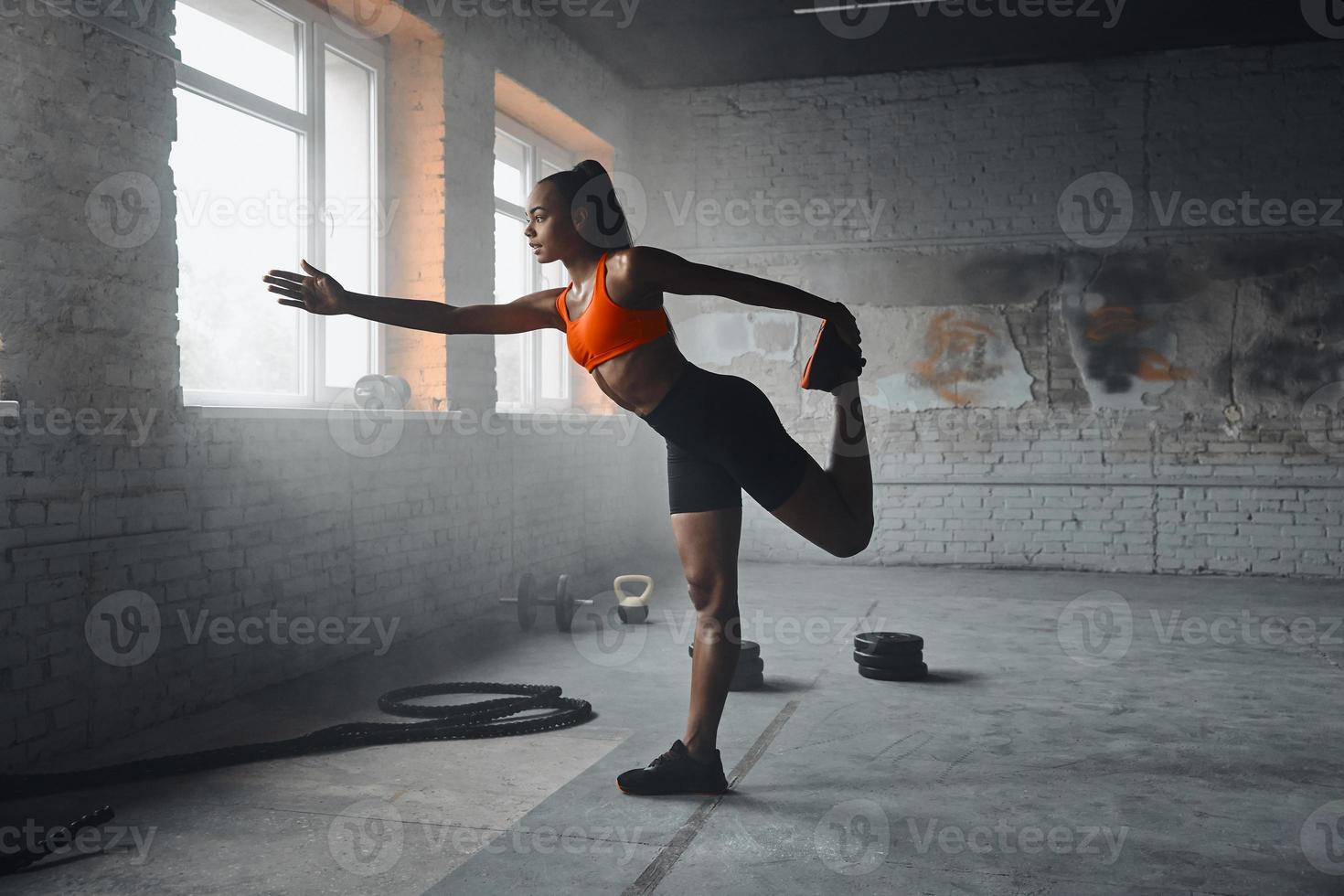 Attractive young African woman in sports clothing doing stretching exercises in gym photo