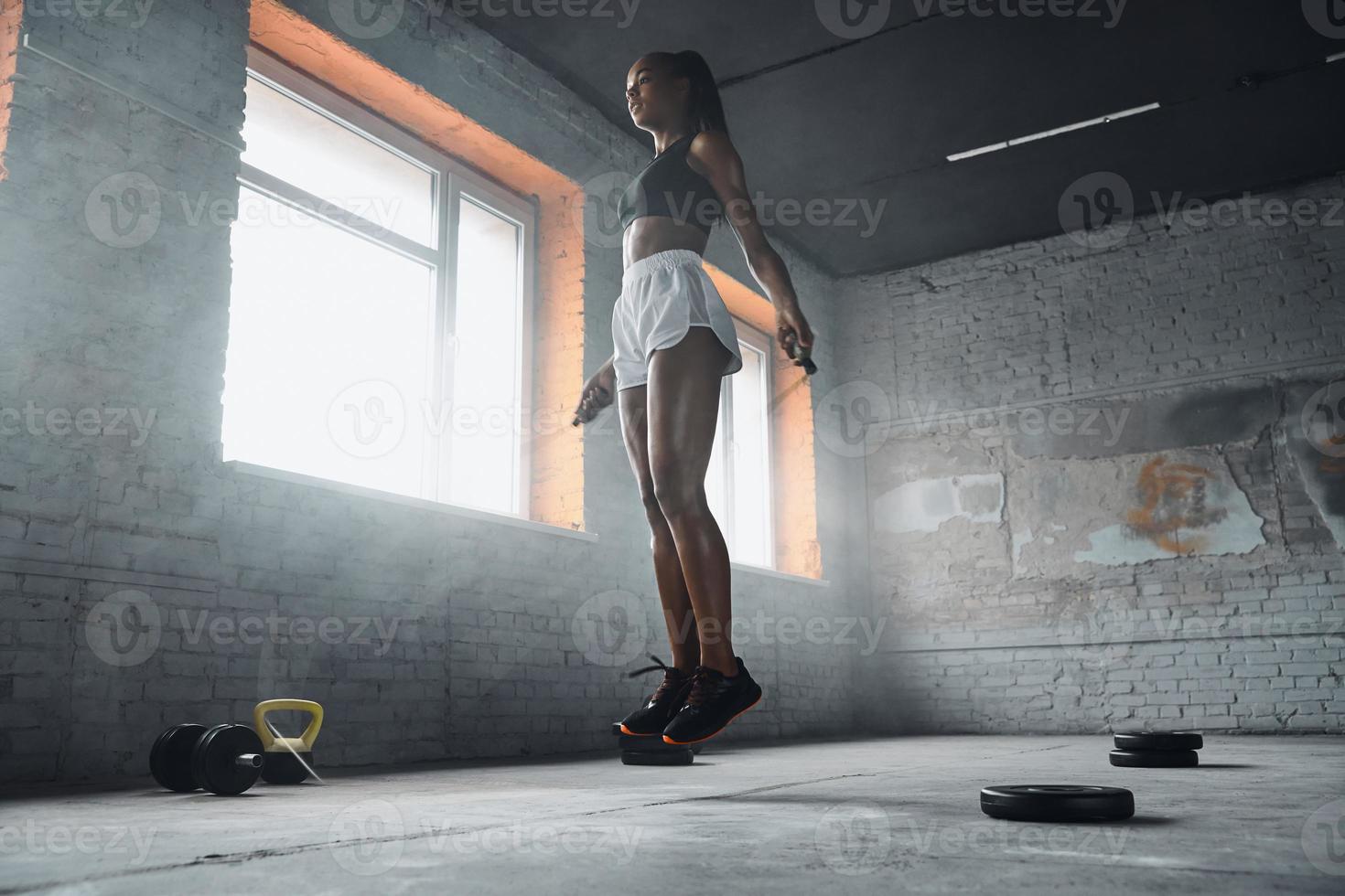 Full length of beautiful young woman jumping with rope in gym photo