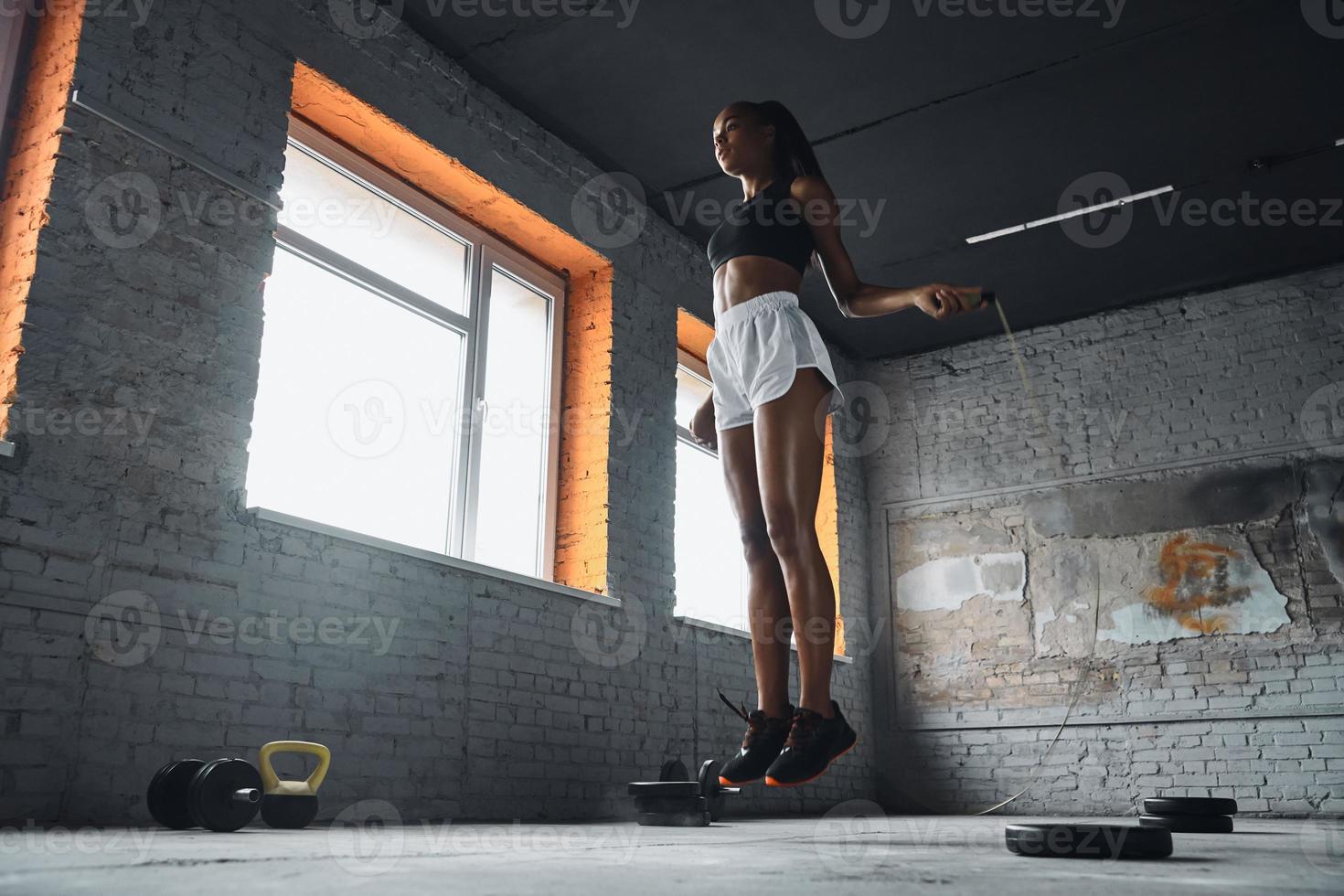 Full length of confident young woman jumping with rope in gym photo