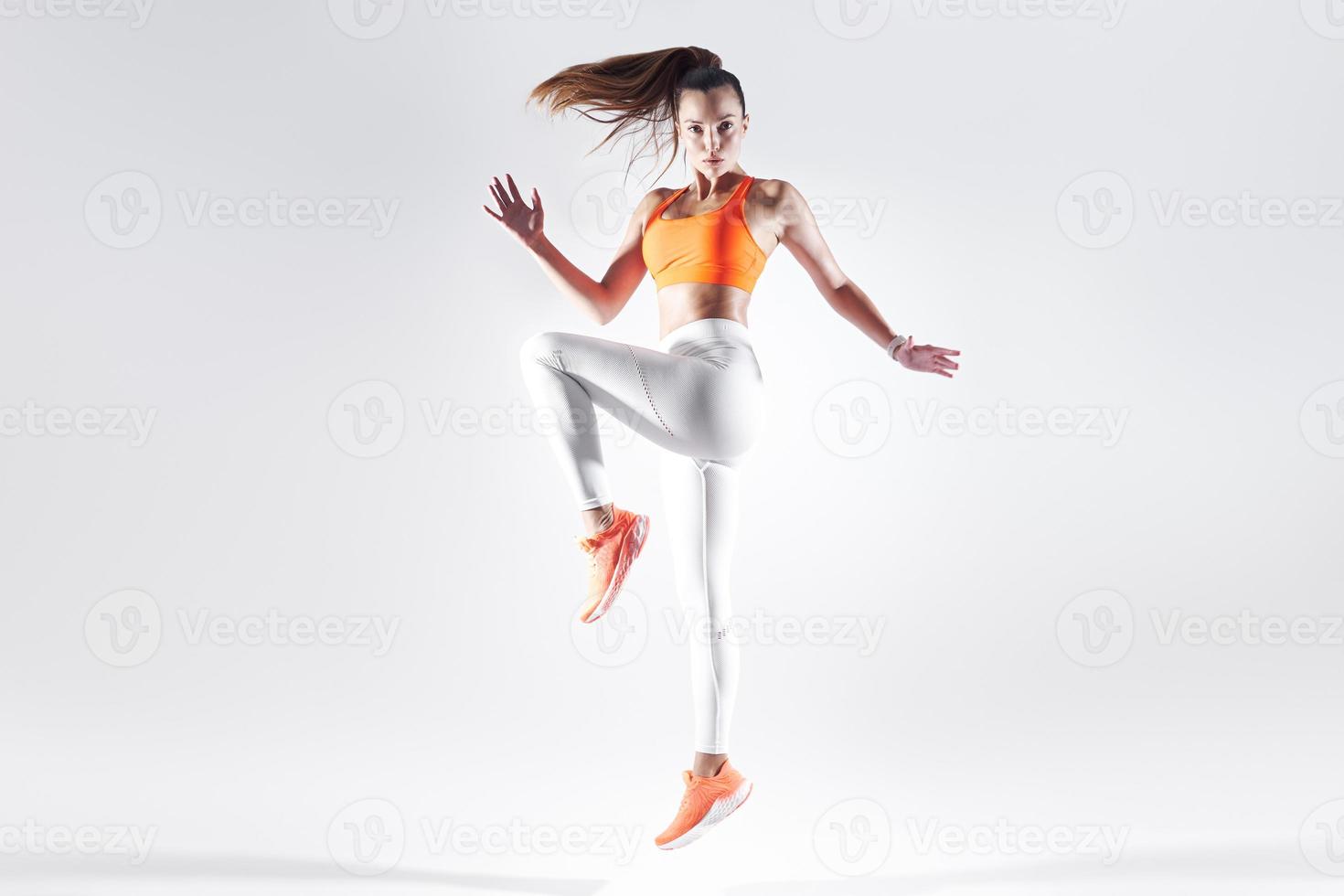 Beautiful young woman in sports clothing jumping against white background photo