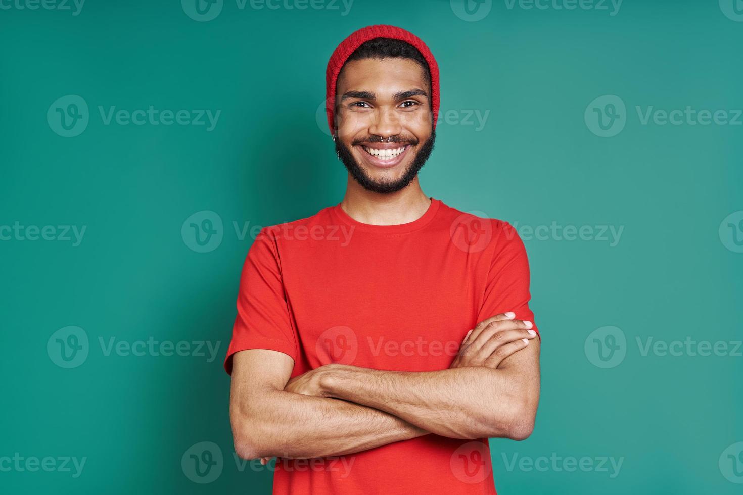 Happy African man keeping arms crossed and smiling while standing against green background photo
