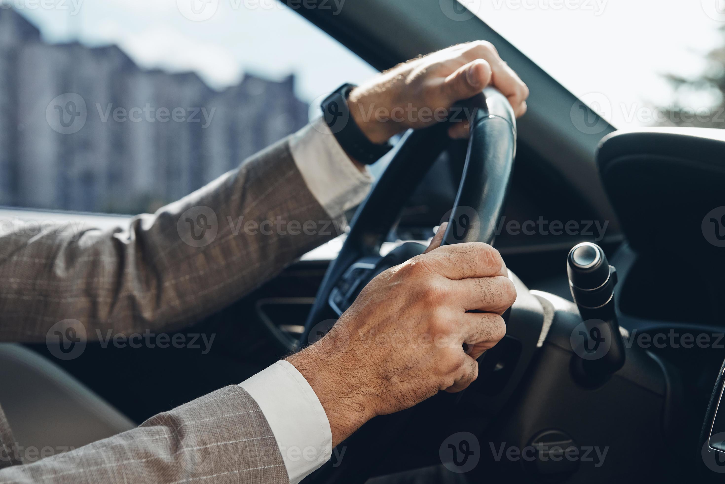 Closeup of man holding hands on steering wheel while driving a car