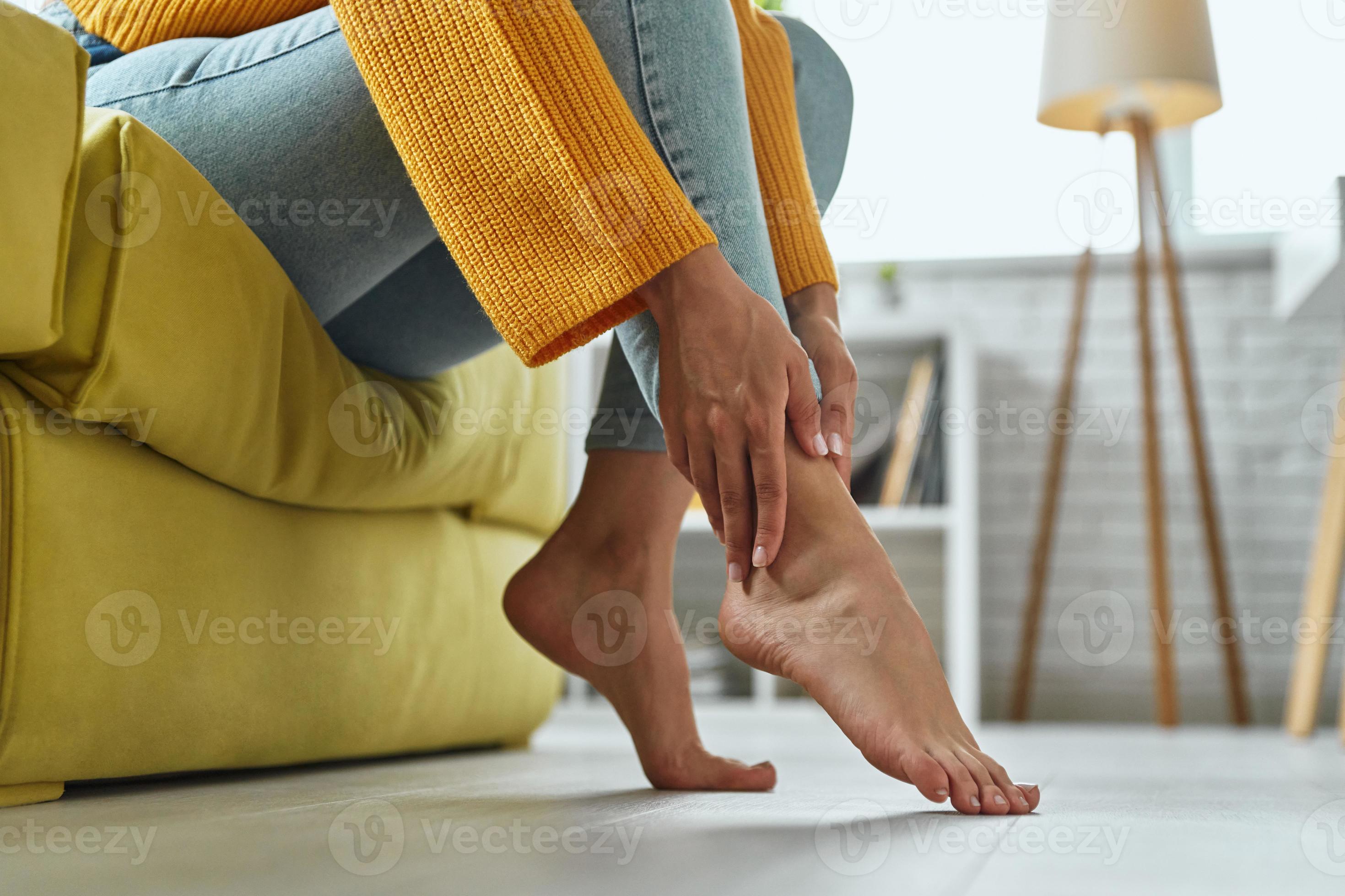 Closeup of woman massaging her tired feet while sitting on the couch