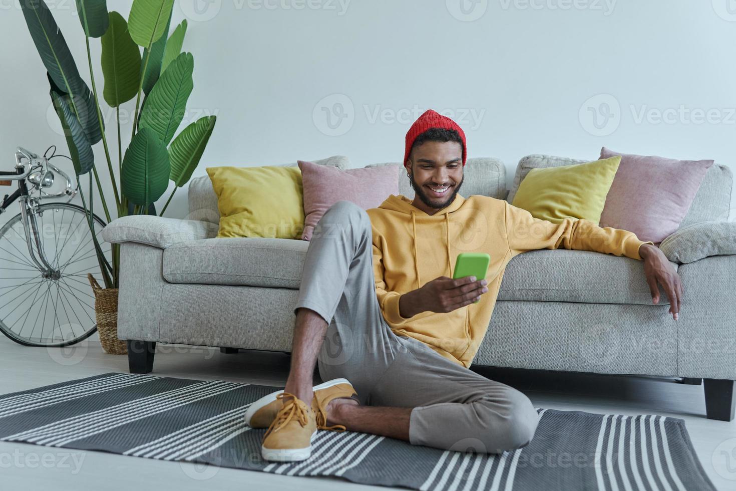 Relaxed young African man using smart phone while sitting on the floor at home photo