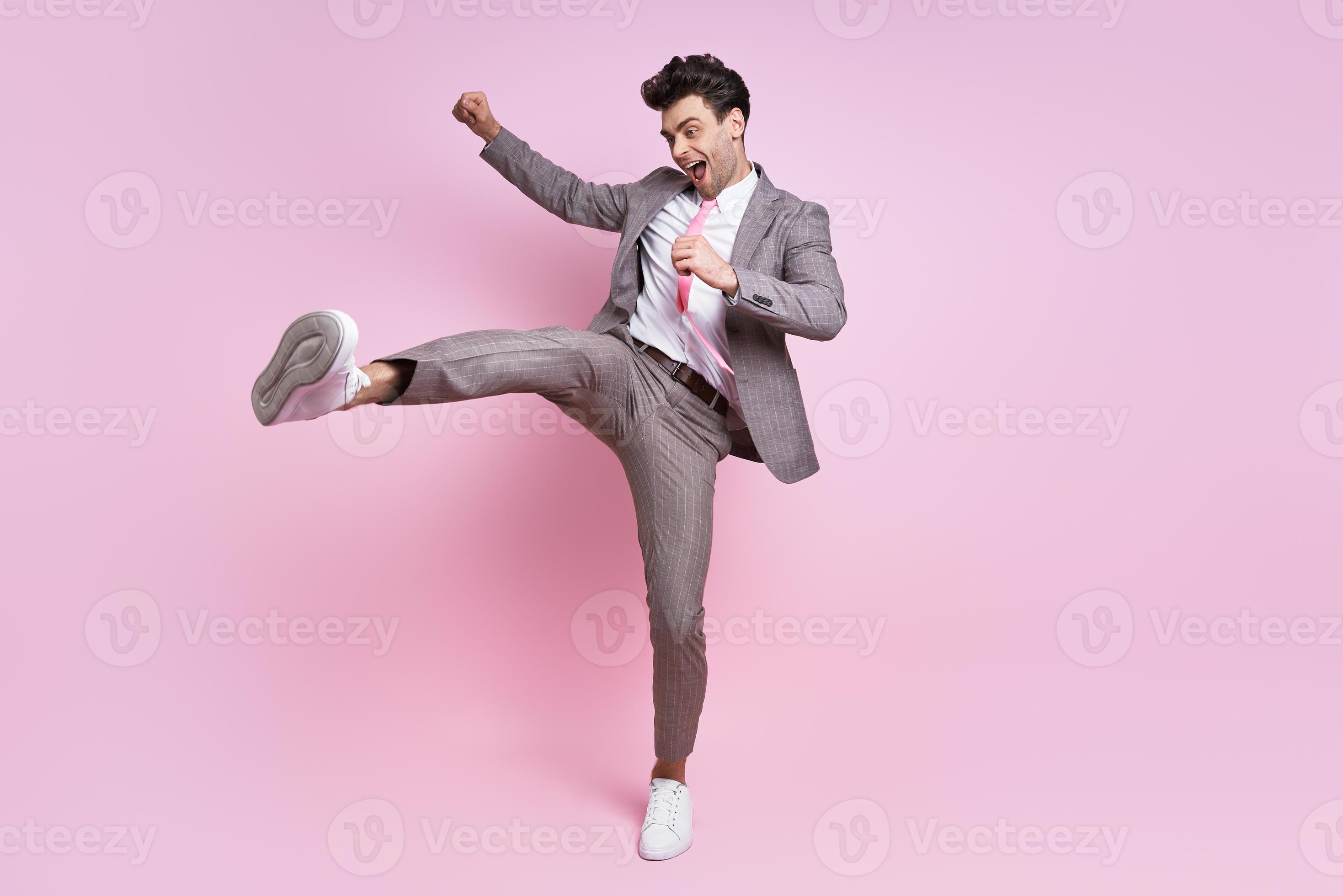 Excited young man in full suit throwing leg kick while standing against