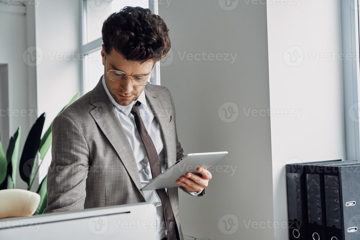 joven concentrado que usa una tableta digital mientras trabaja en la oficina foto