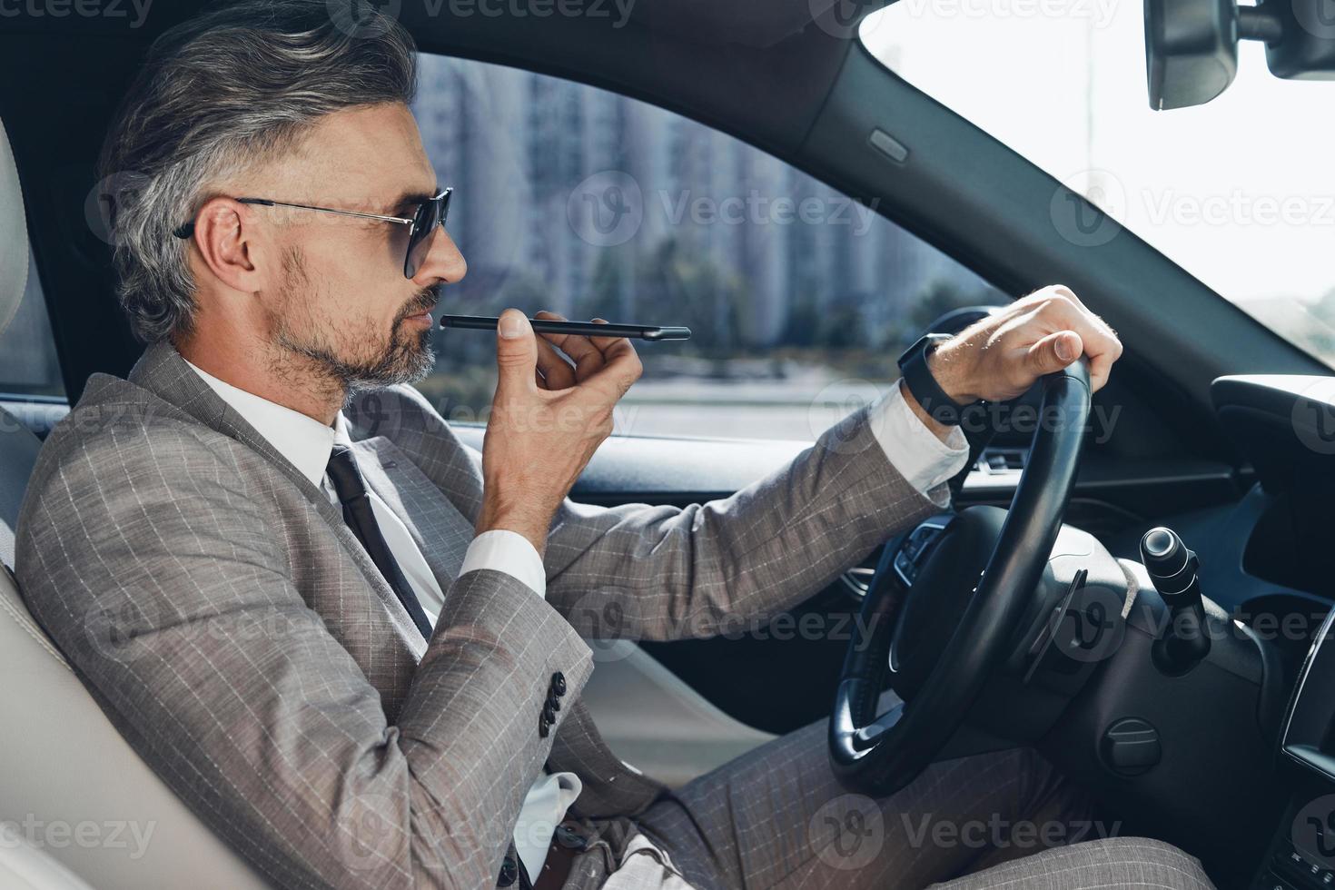 Mature man in formalwear using loudspeaker while talking on mobile phone from car photo