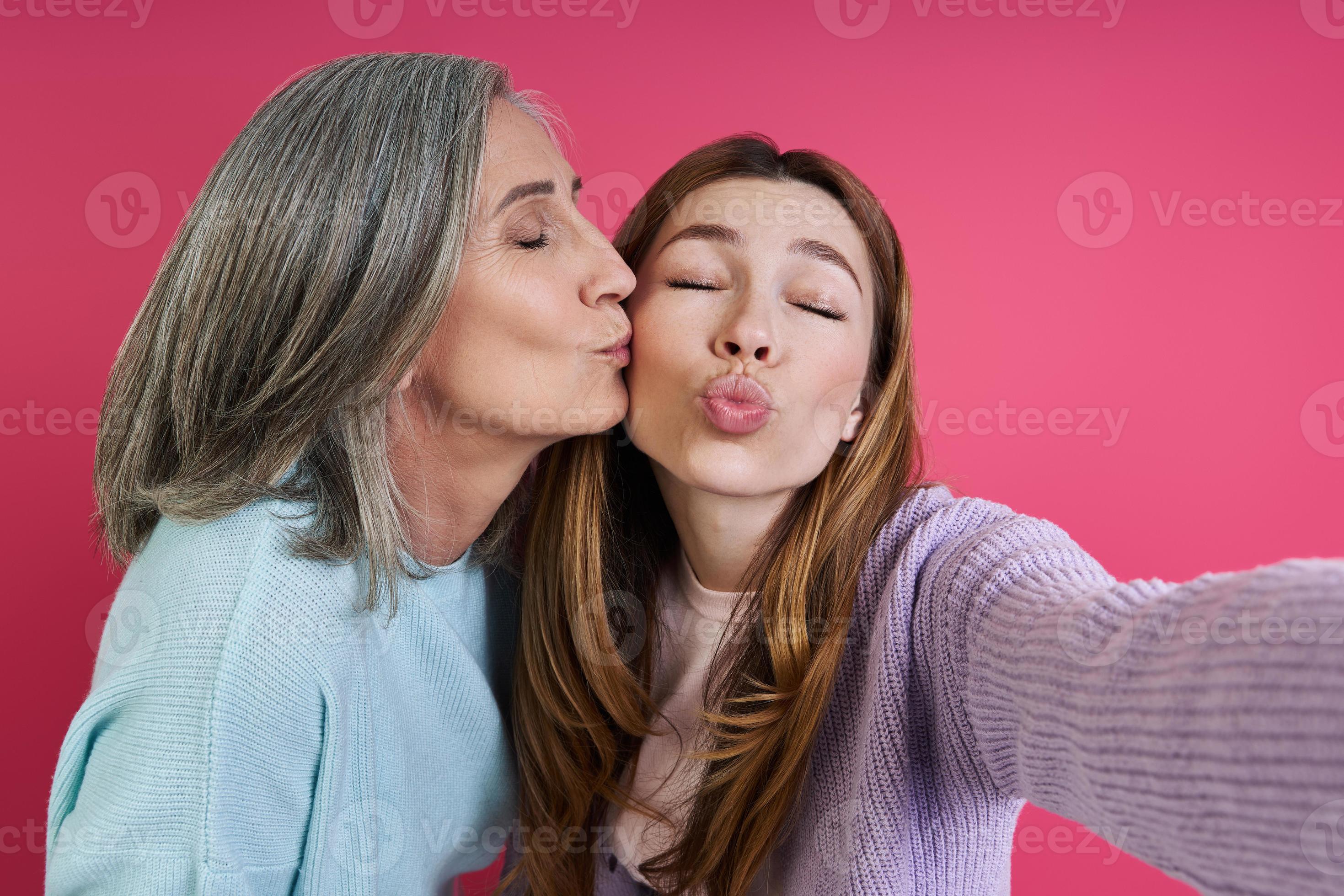 Senior mother kissing her adult daughter while making selfie against pink background 10154129 Stock Photo at Vecteezy photo
