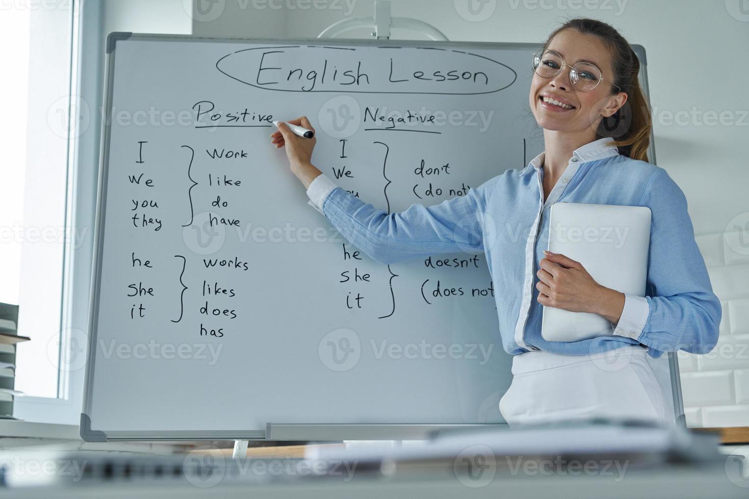 Happy young woman pointing whiteboard while standing at the classroom photo