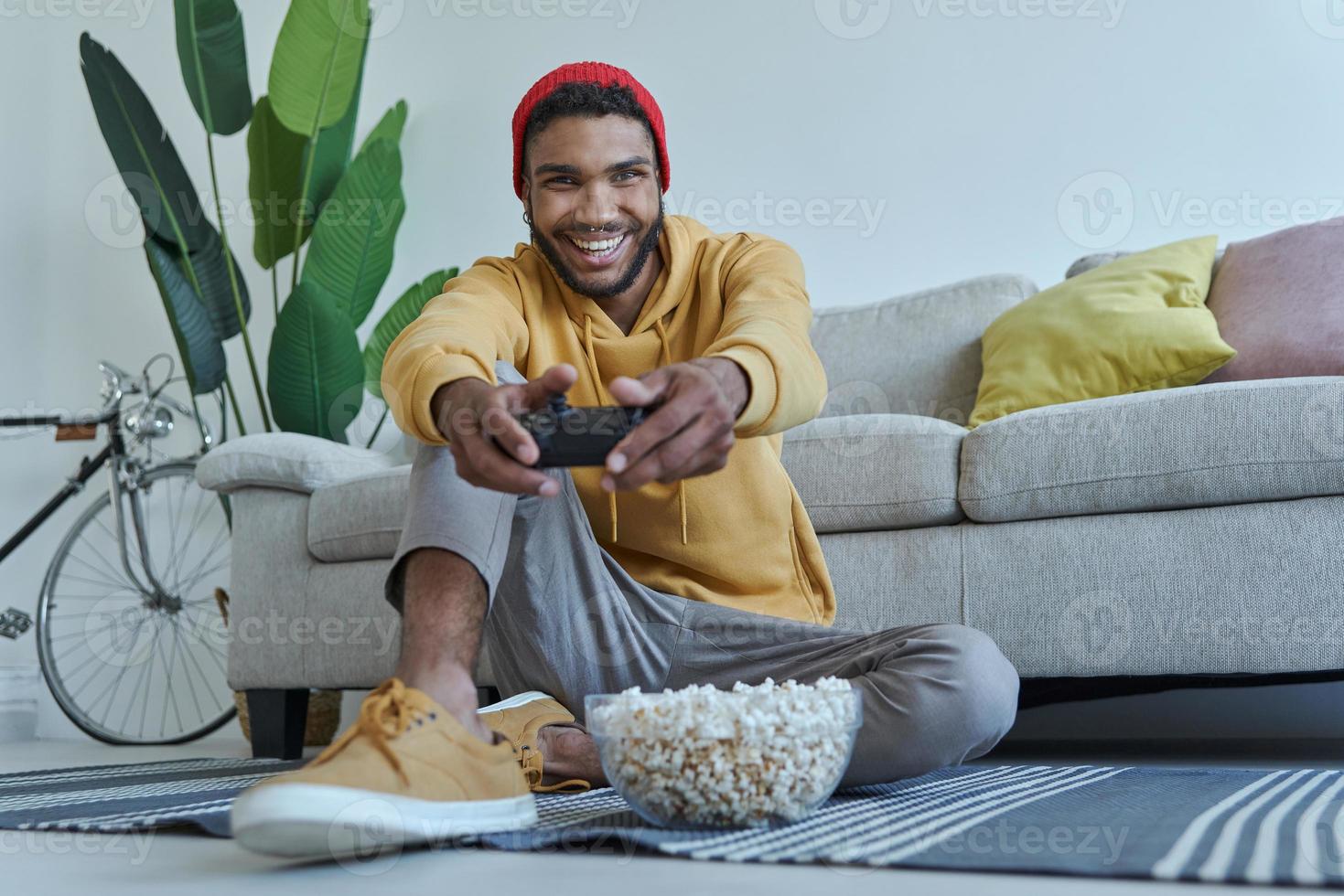 Joyful young African man playing video games while sitting on the floor