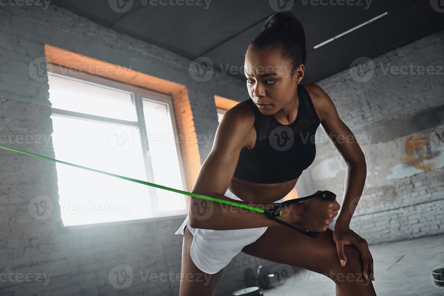Beautiful young African woman exercising with elastic resistance band in gym photo