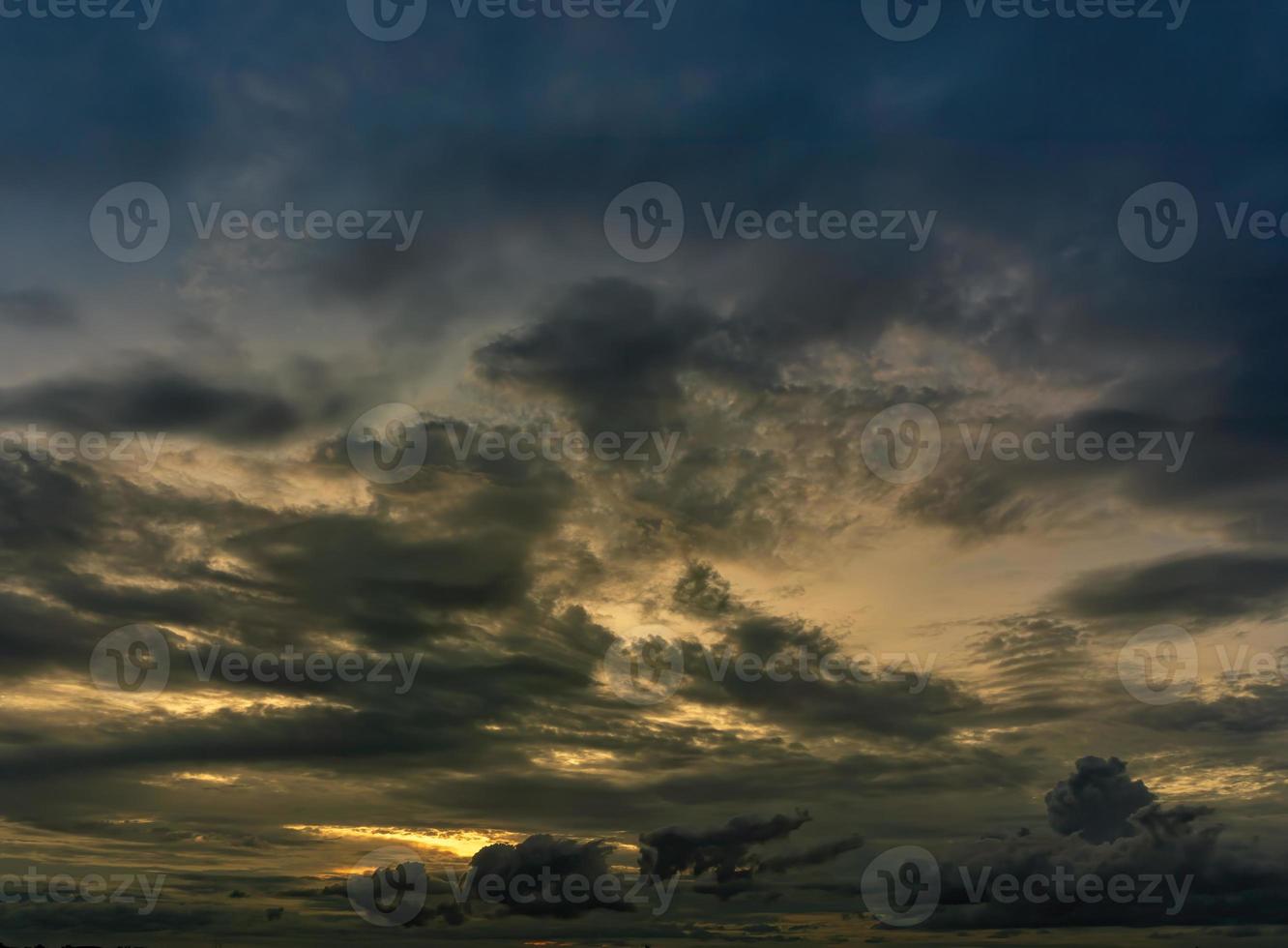 The clouds filled the sky, obscuring the light from the sun during the sunset. The sky in the middle is coloured orange from the sun. The bottom and top sky are black and dark  rain clouds. photo