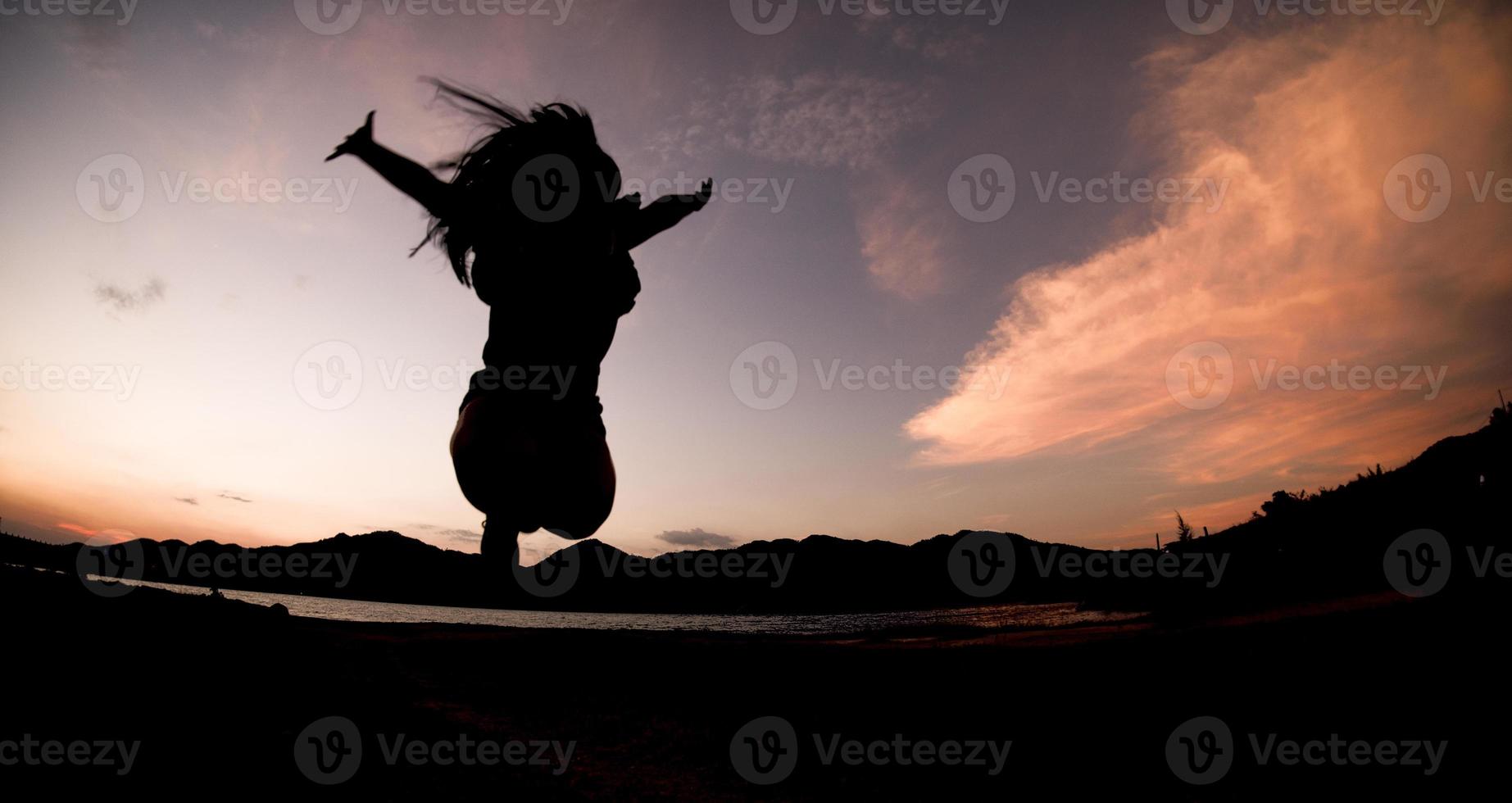 silueta, feliz saltando sombra chica salta sobre el cielo naranja por la noche foto