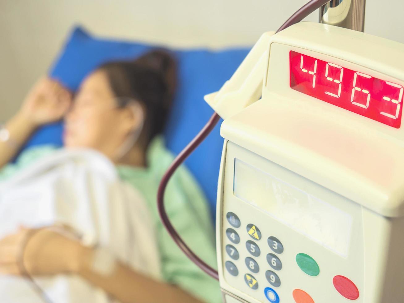 A lady patient is sleeping while putting blood dripping her arm. Photo is focused at medical instrument digital machine.