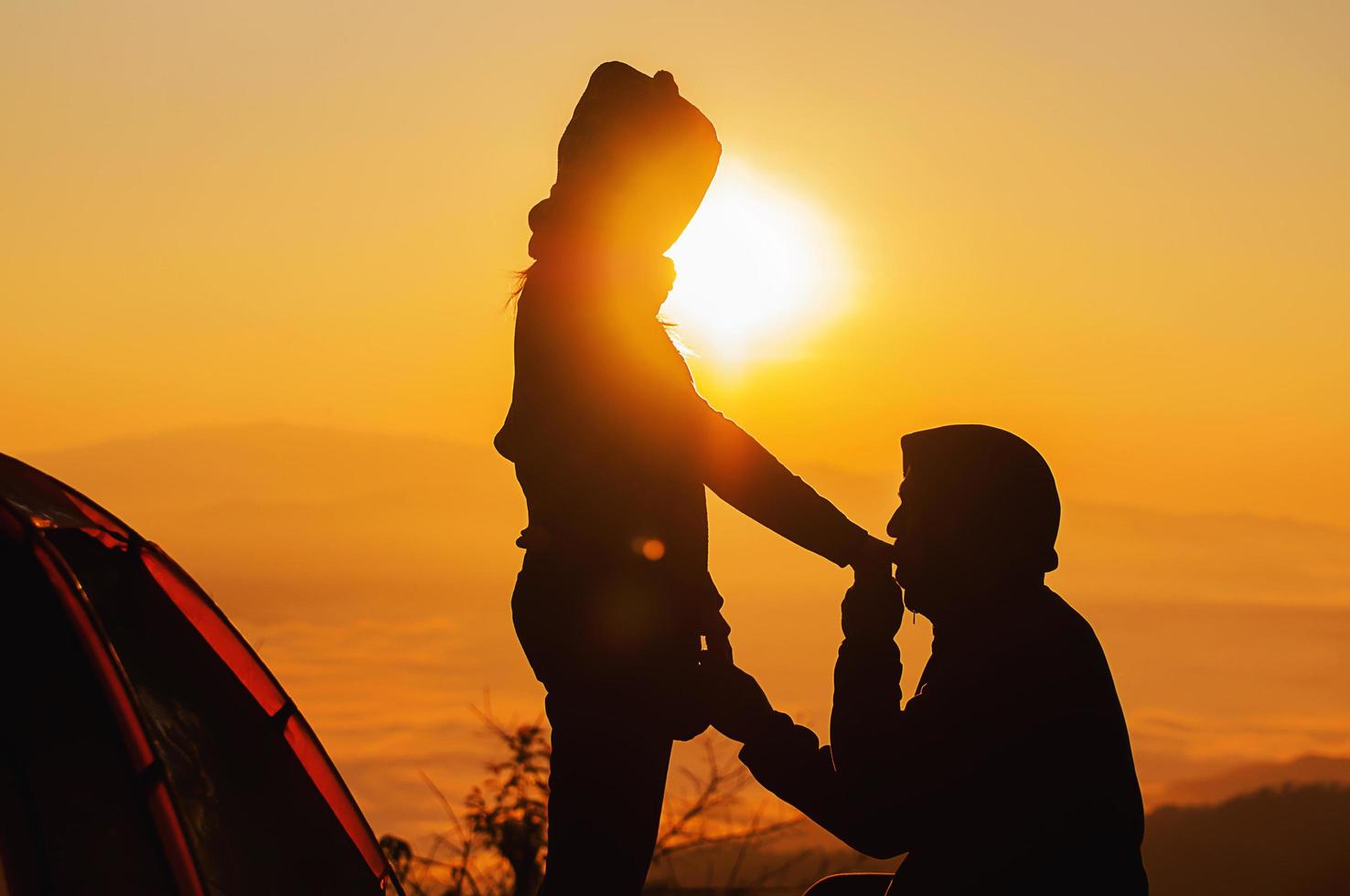 silhouette couple love concept - man hold and kiss woman hand in warm morning sun silhouette during his camping with sea of mist or fog in high mountain area of chiang mai north of thailand photo