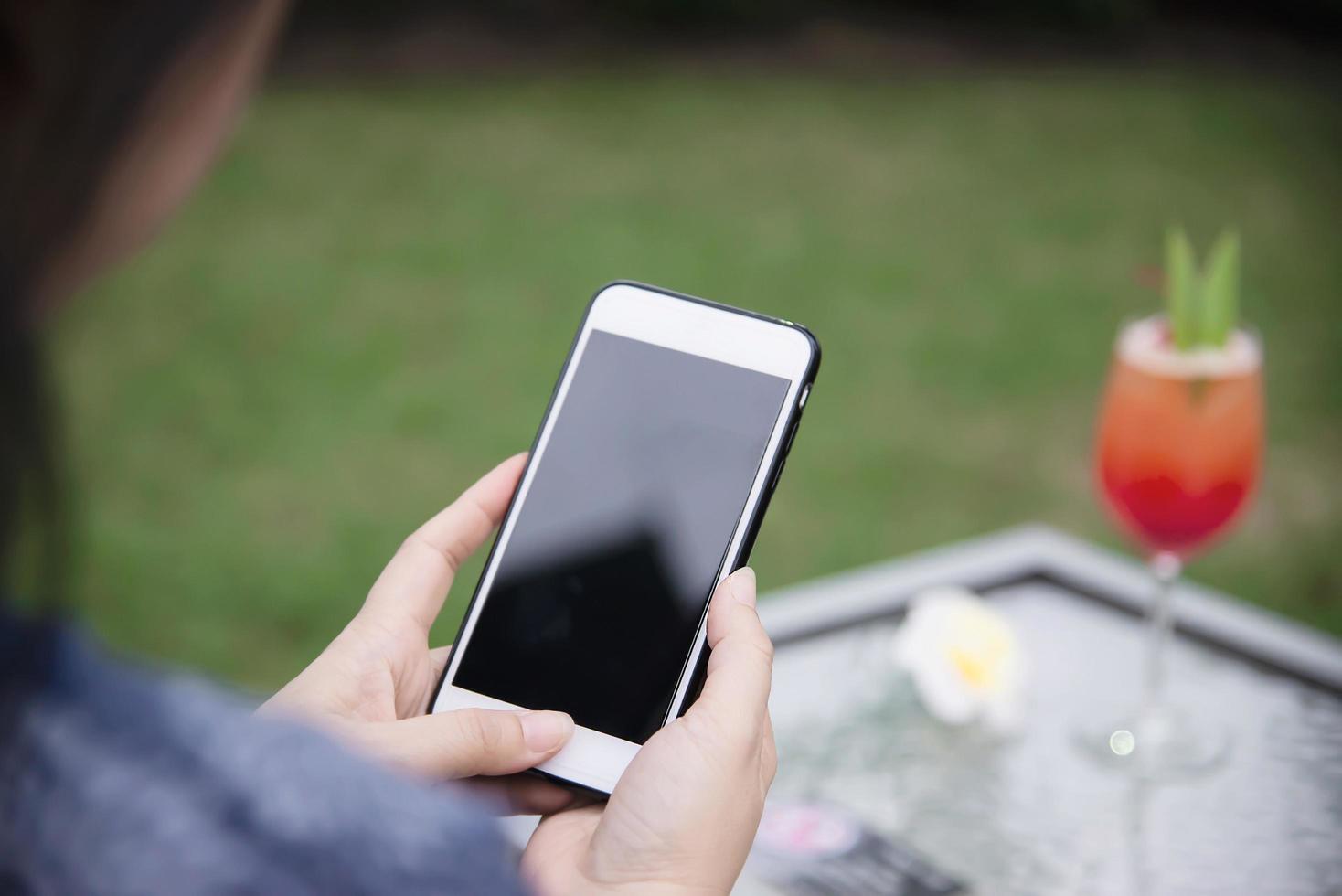 Lady using mobile phone relax in green garden with soft drink background - people and technology lifestyle concept photo