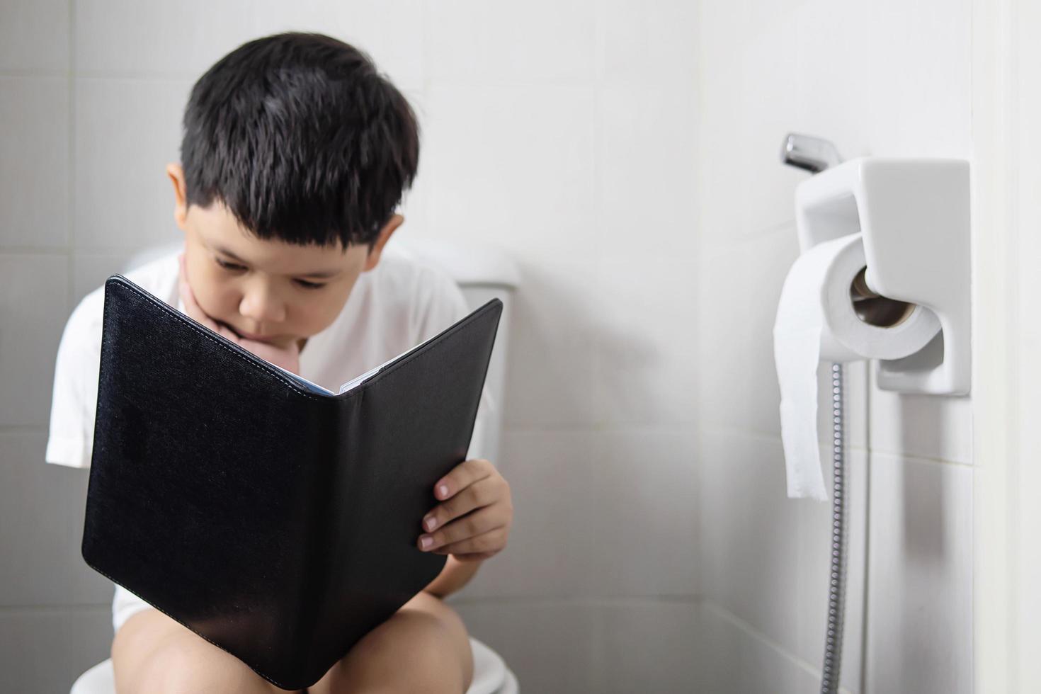 Asian boy sitting on toilet bowl while reading book - health problem concept photo