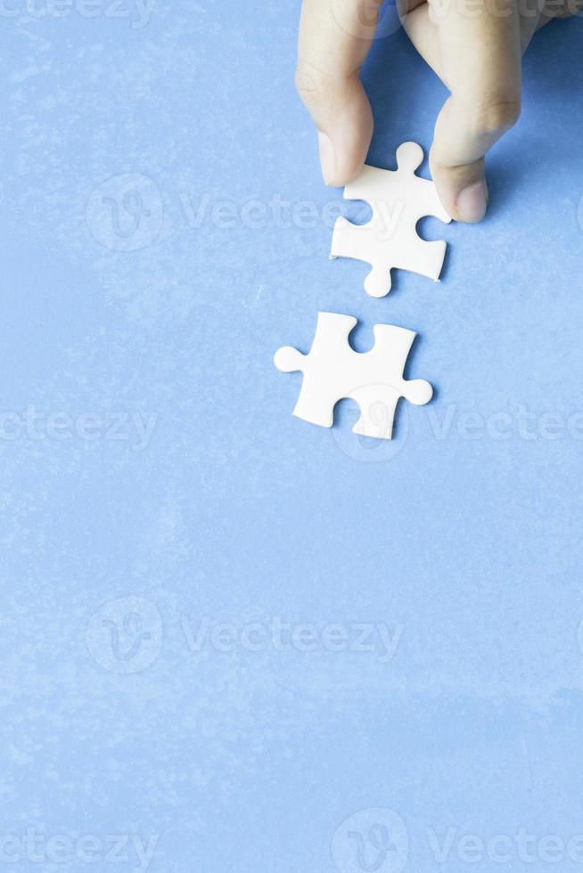 Close up hand holding and playing jigsaw game incomplete. White part of jigsaw puzzle pieces on blue background. concepts of problem solving, business, teamwork, Texture photo with copy space for text