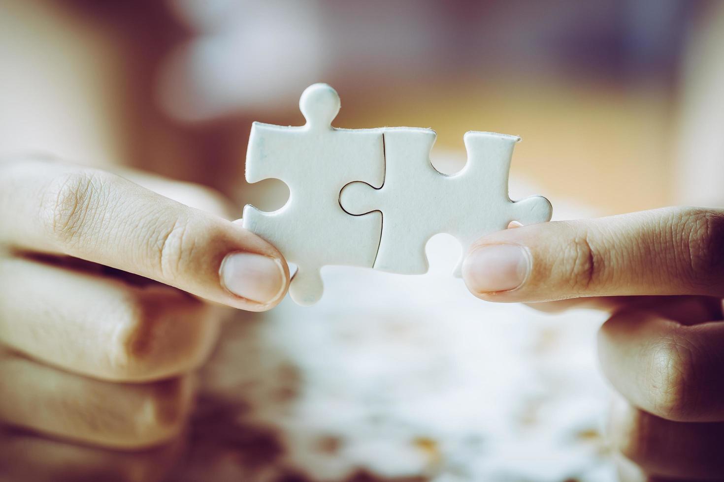 Hands of a person little child and parent playing jigsaw puzzle piece game together on wooden table at home, concept for leisure with family, play with children's development, education and fun. photo
