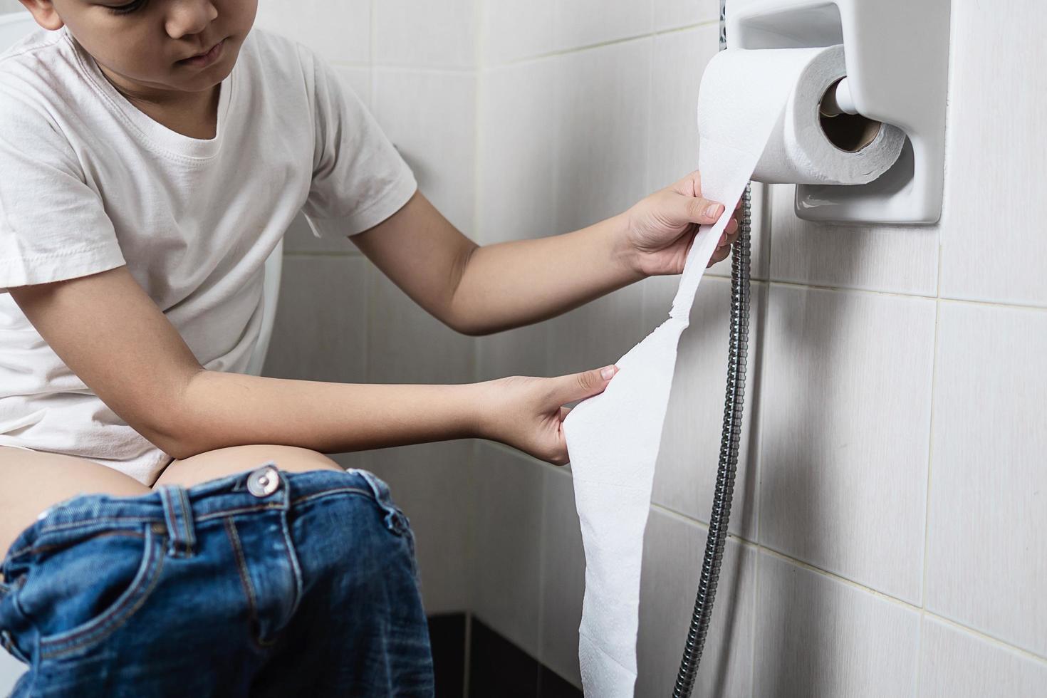 Asian boy sitting on toilet bowl holding tissue paper  - health problem concept photo