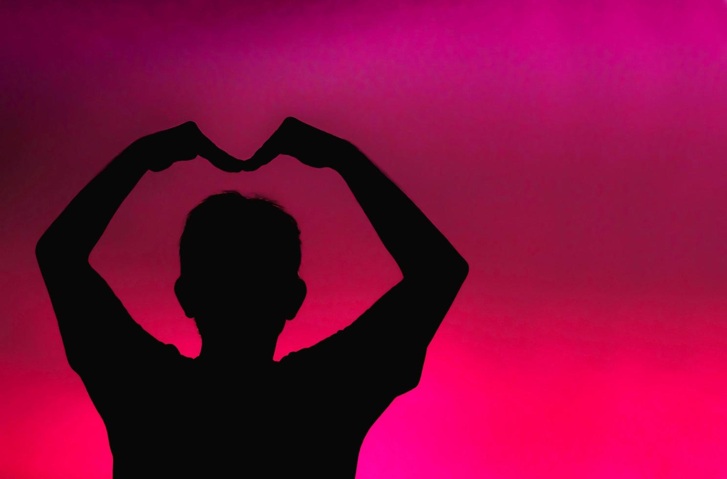 silueta de hombre haciendo forma de corazón sobre fondo rosa foto