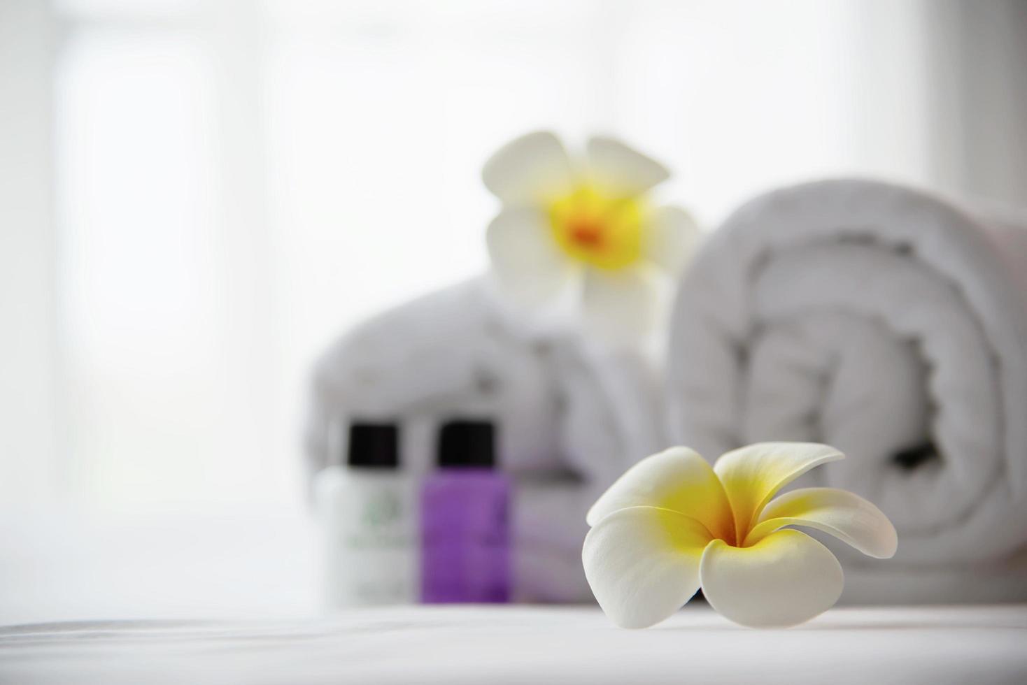 Hotel towel and shampoo and soap bath bottle set on white bed with plumeria flower decorated - relax vacation at the hotel resort concept photo